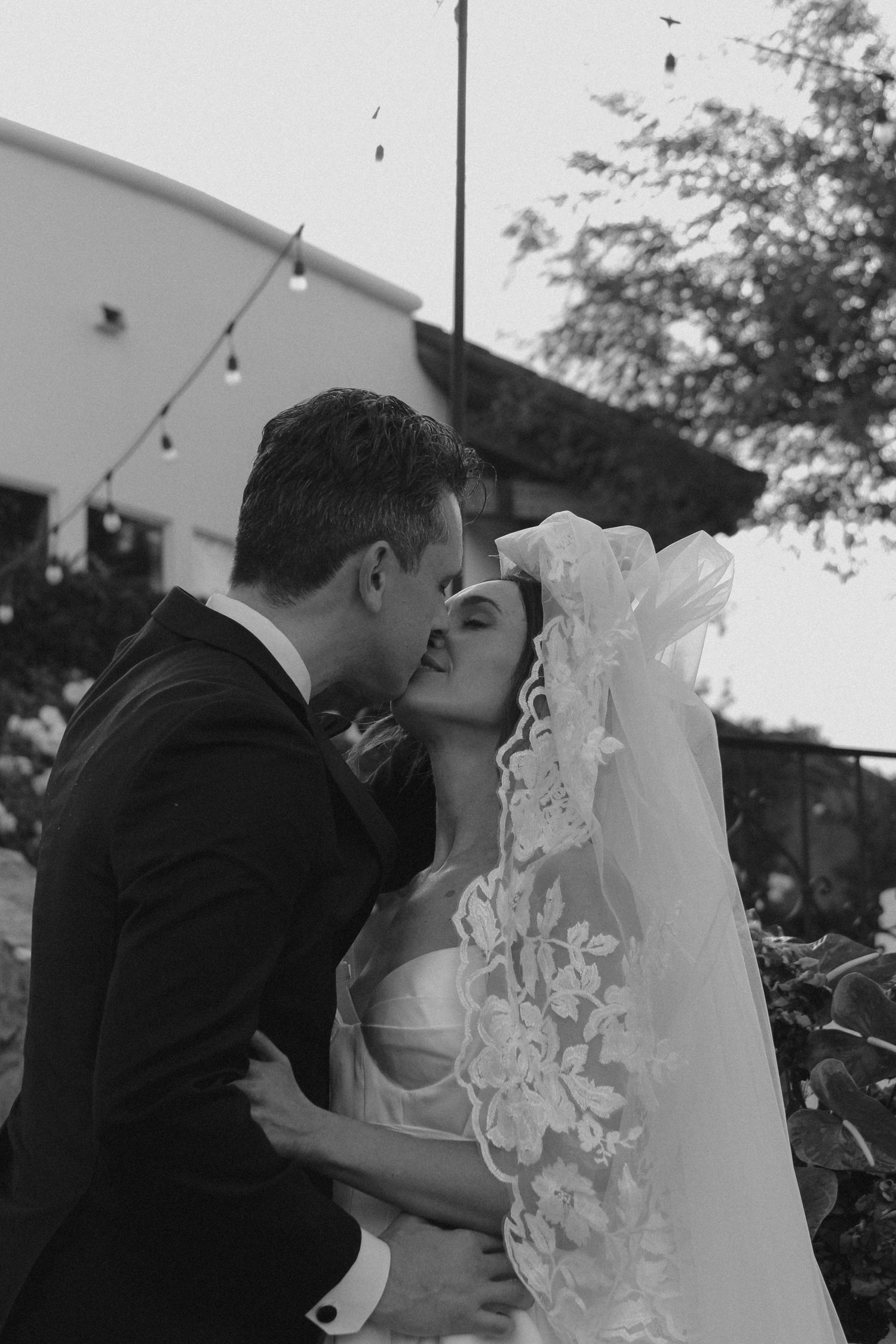 A romantic black and white wedding photo capturing a tender kiss between newlyweds with a flowing lace veil.