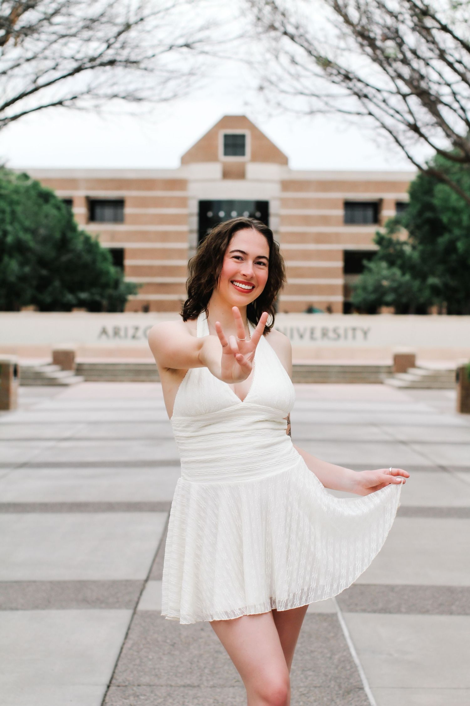 Graduate in white dress celebrates at university campus courtyard.