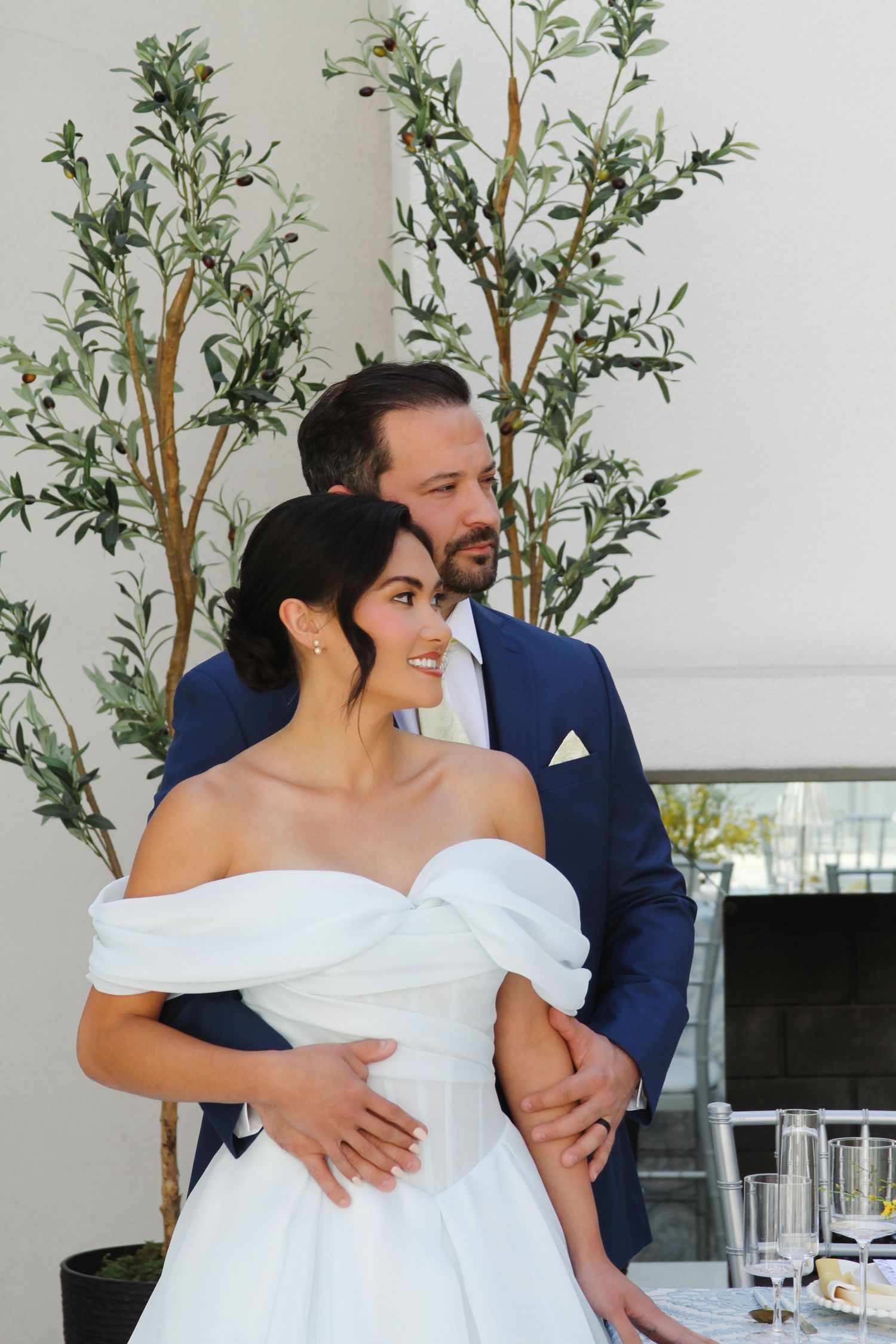 A tender wedding moment captured against decorative potted plants and white walls.