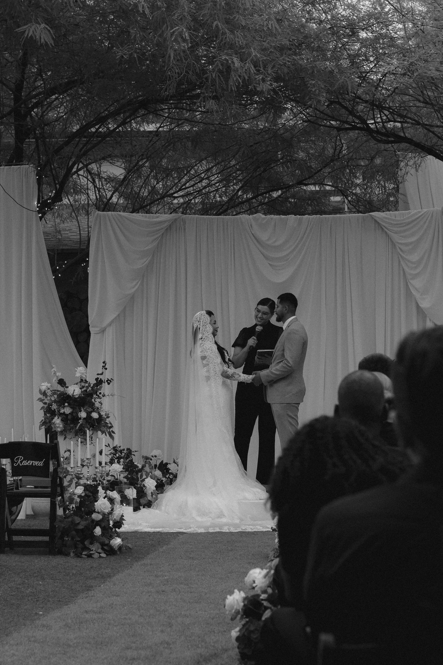 A black and white photo of an outdoor wedding ceremony with white drapes and guests seated in rows. Tyler Garlej Photography
