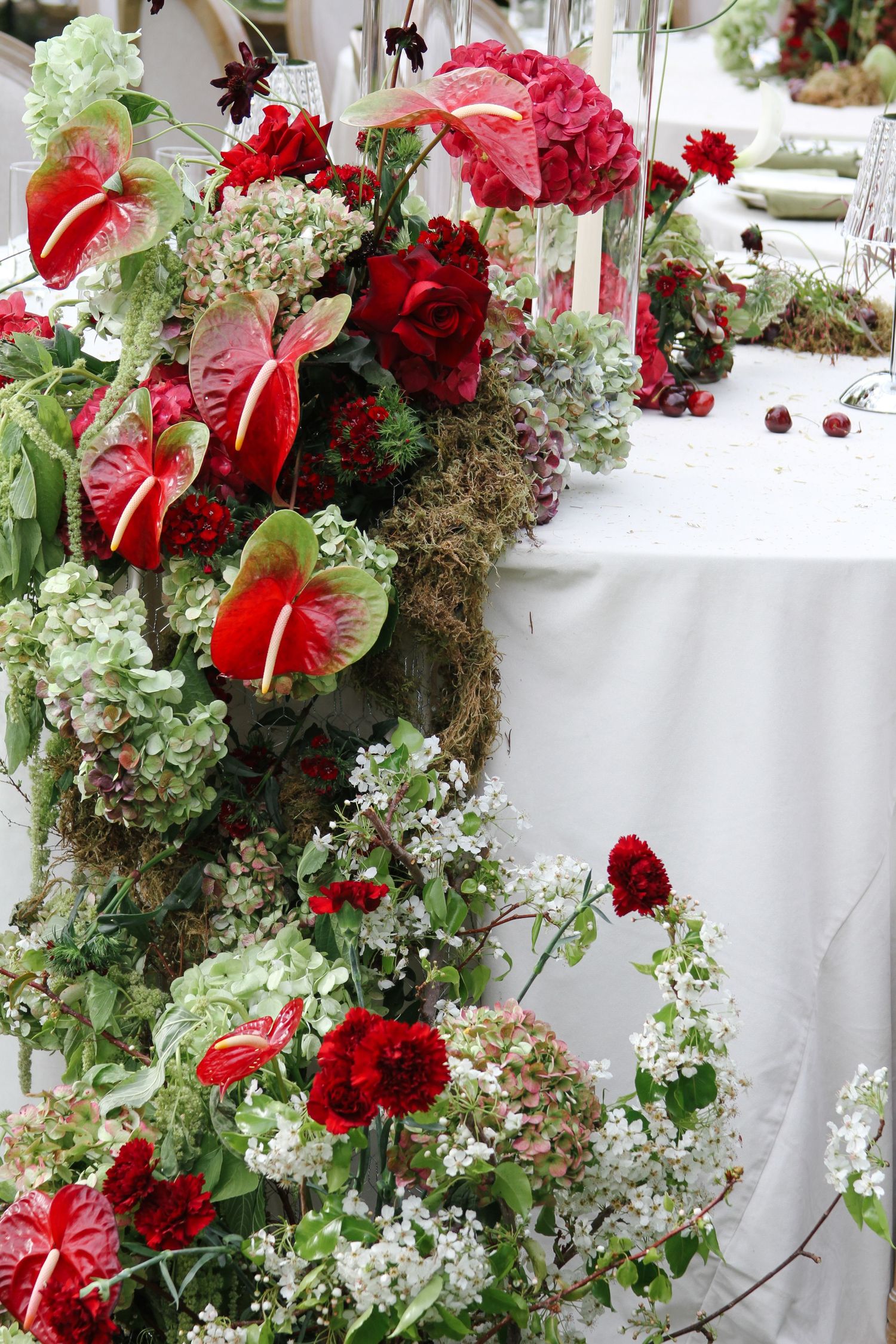 Elegant floral arrangement featuring red anthurium flowers, roses, and cascading greenery against a white backdrop. Tyler Garlej Photography