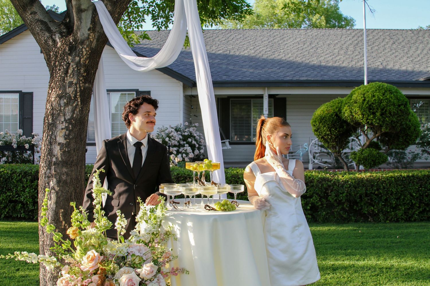 Bride and groom standing at a champagne tower table during an outdoor garden wedding reception.