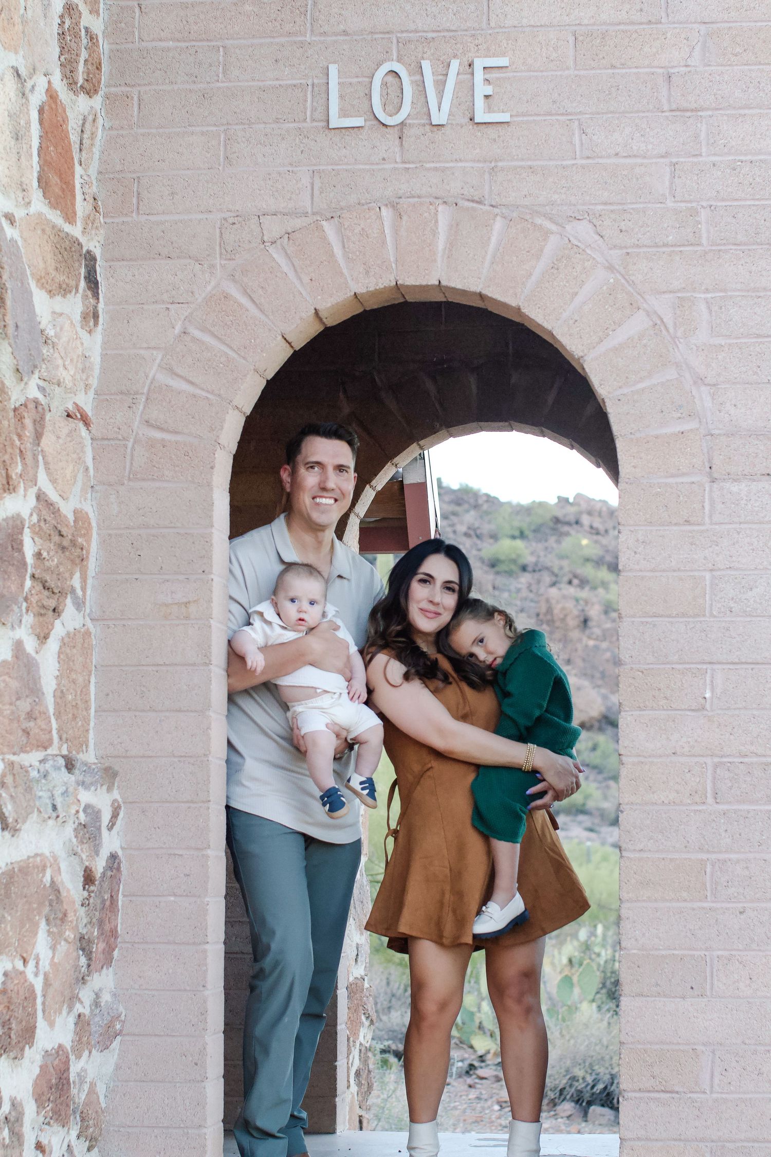 A family poses for photos in front of an arched brick wall with the word 'LOVE' displayed above.