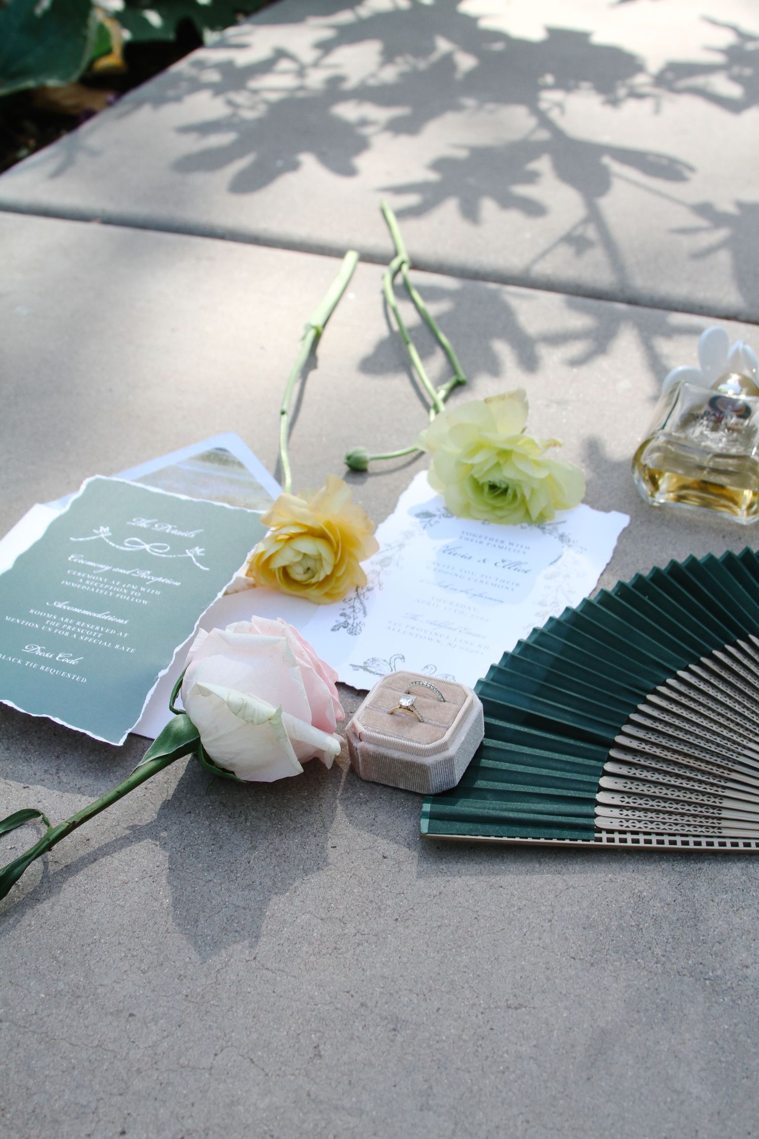 Wedding invitations with green paper fans and delicate floral decorations arranged on a gray surface. Tyler Garlej Photography