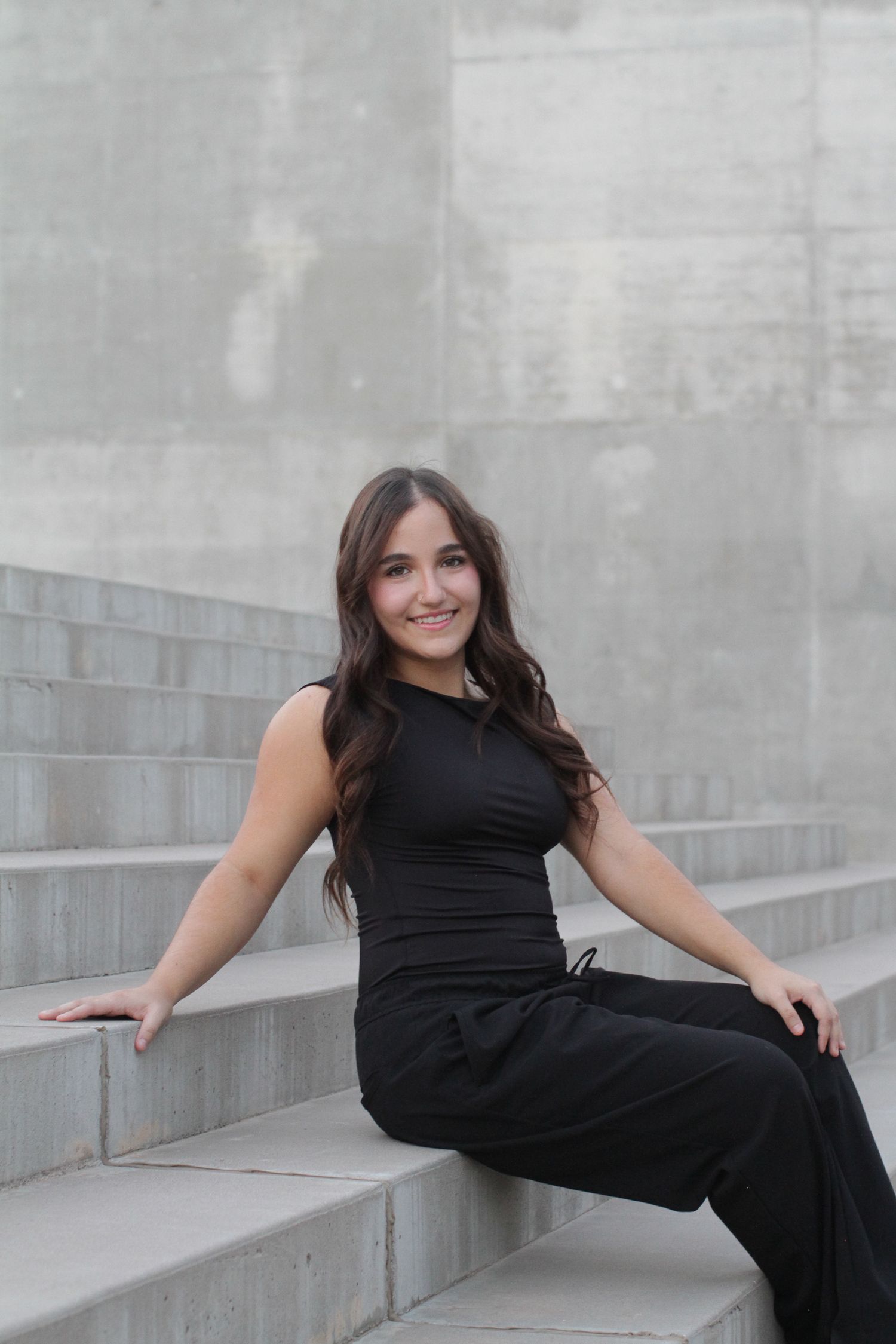 Person wearing black outfit poses elegantly on concrete steps while leaning on railing.