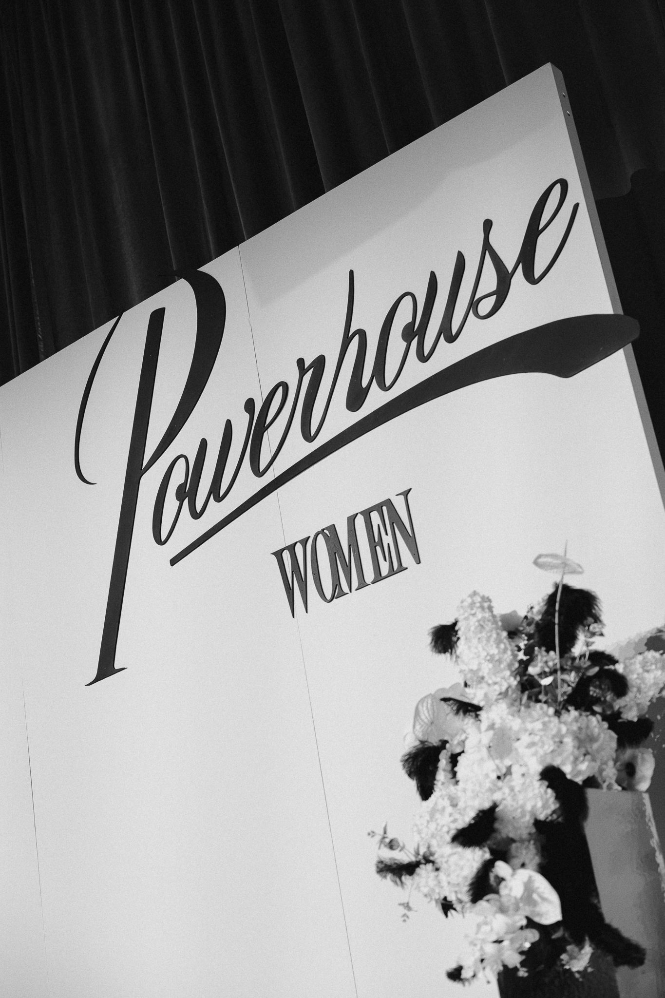 Black and white photo of a Powerhouse Women event sign with elegant script lettering and floral arrangement.