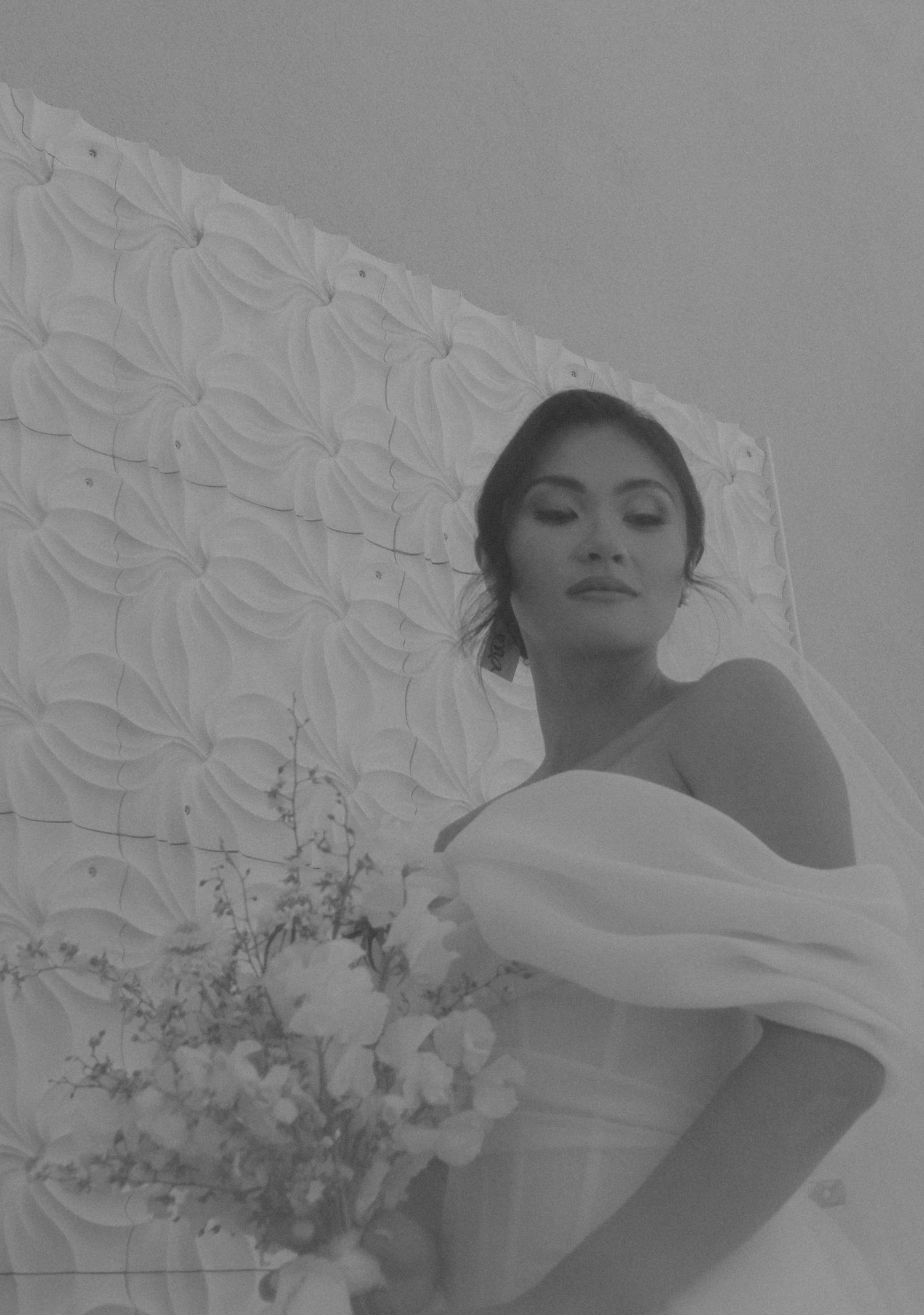 Black and white portrait of a bride in an off-shoulder dress with textured wall background.