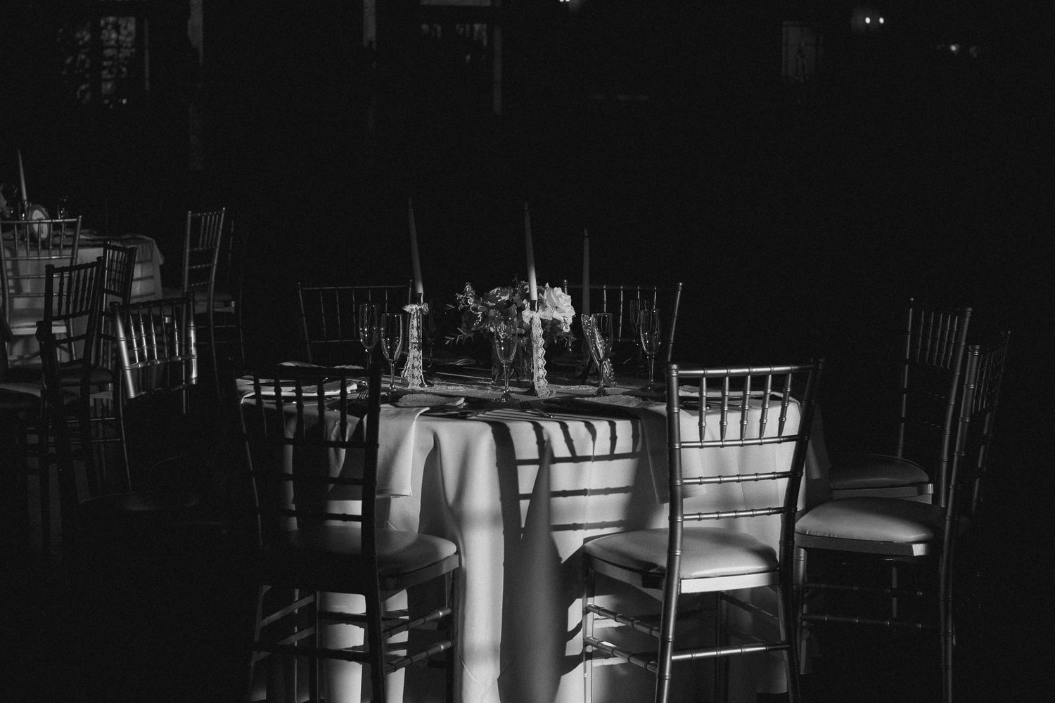 A dark and moody bar interior with empty stools and illuminated bottles on display at night.
