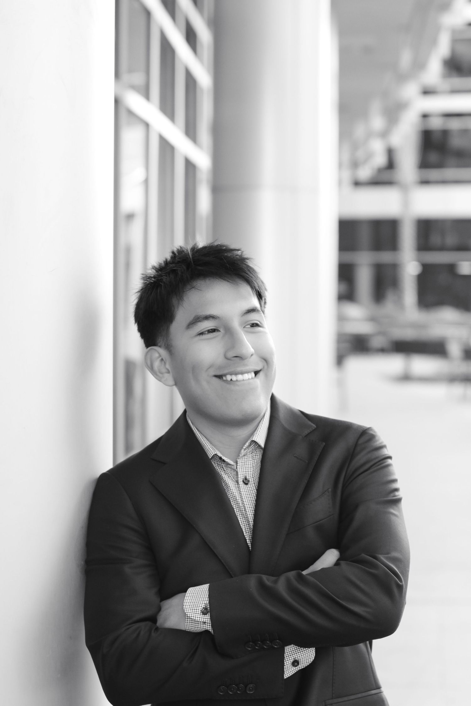 Black and white professional portrait of person in suit jacket smiling against architectural background.