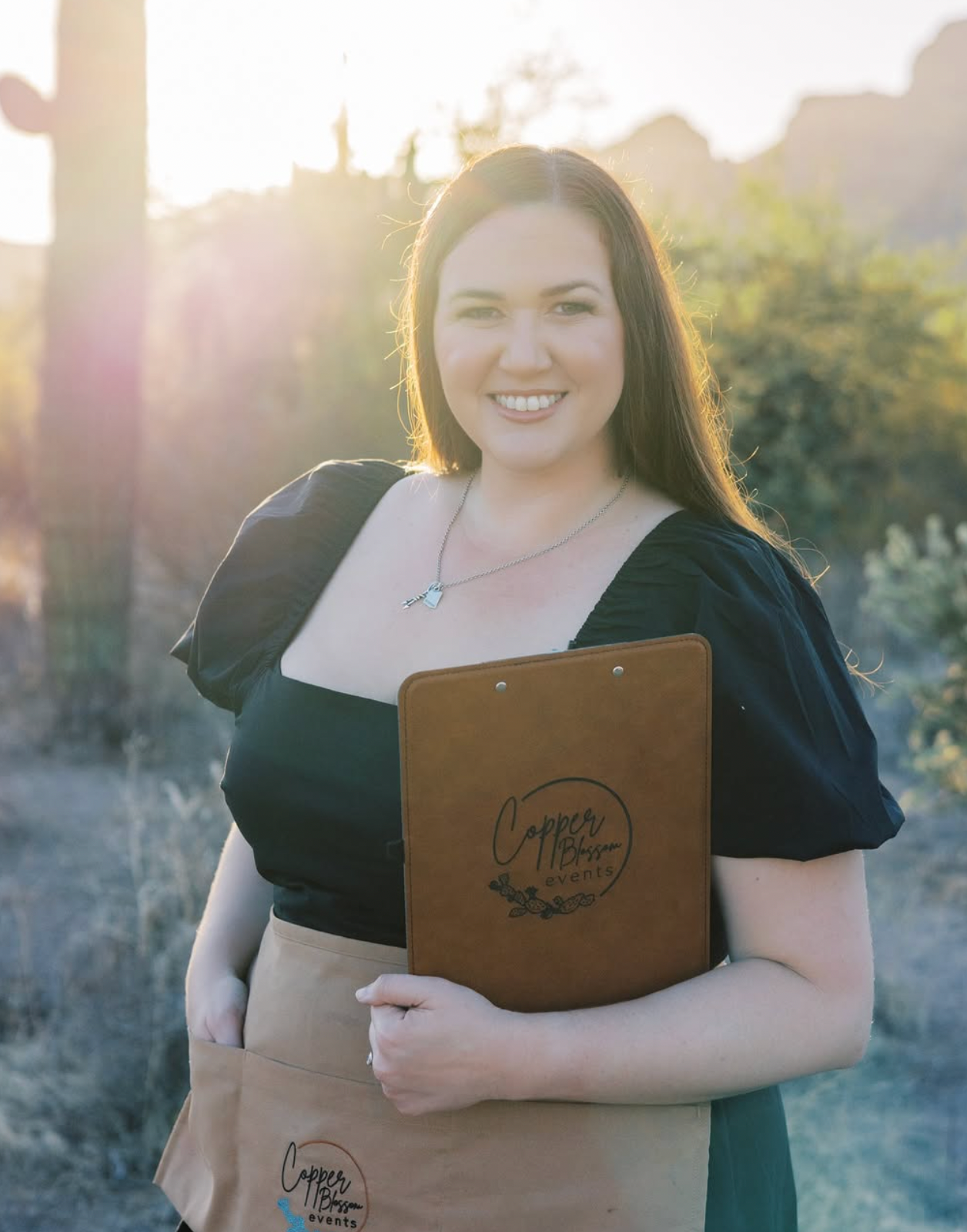 Professional holding leather portfolio outdoors during sunset with desert landscape.