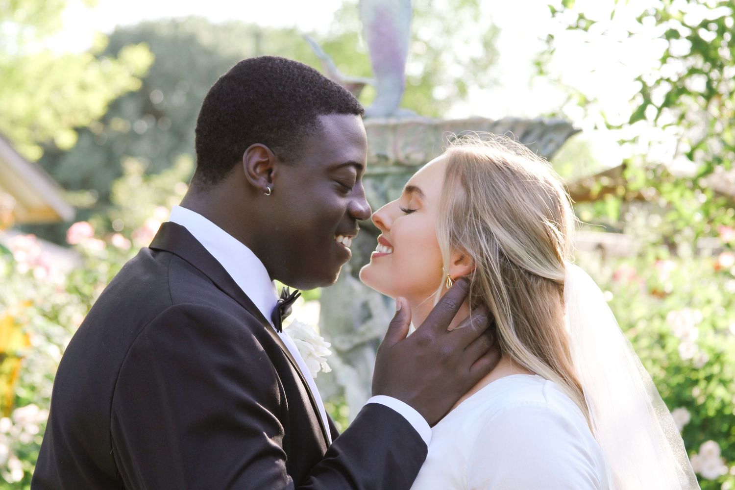 A bride and groom share an intimate moment in a sunlit garden setting.