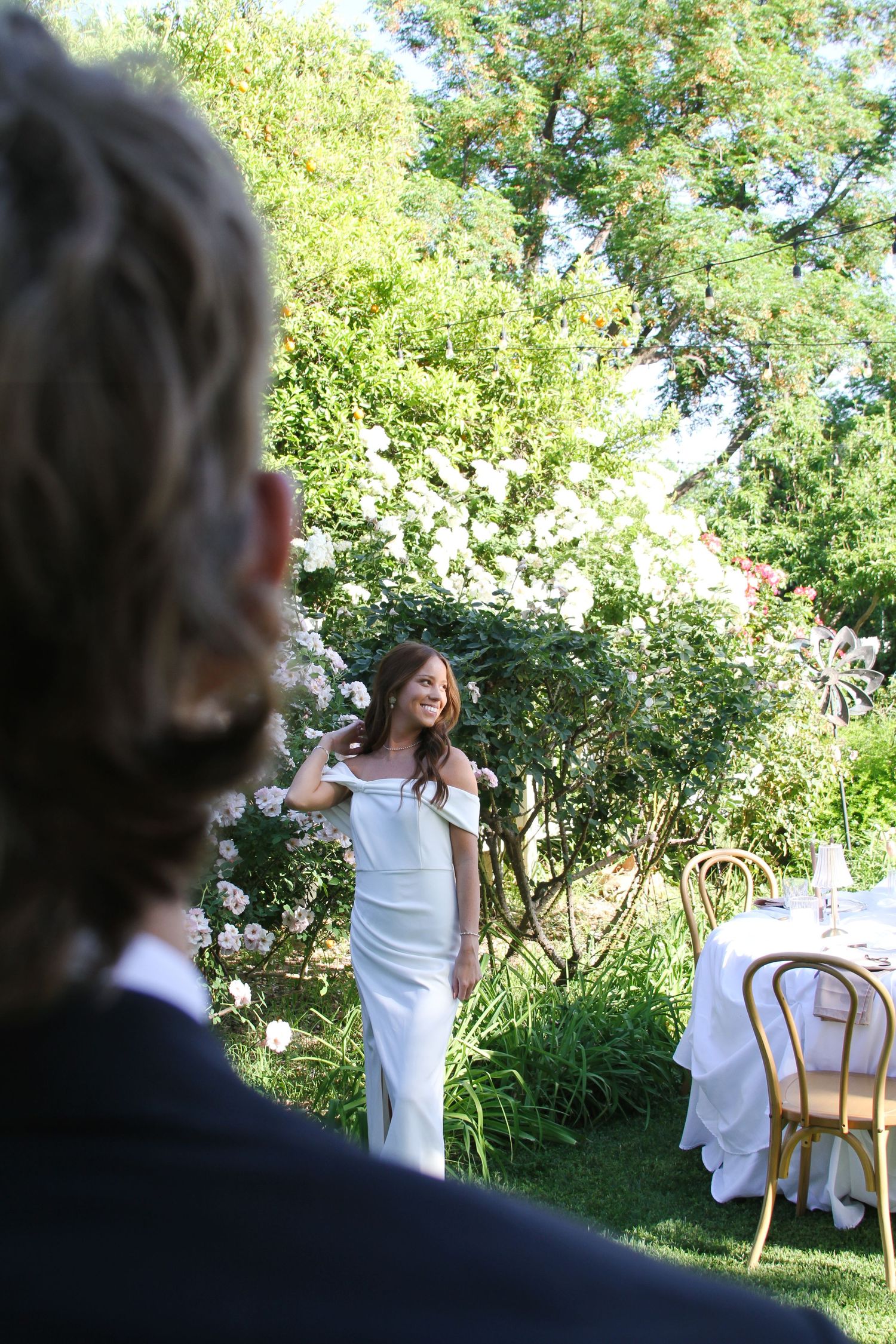 A bride in a white dress stands near an outdoor wedding reception table.