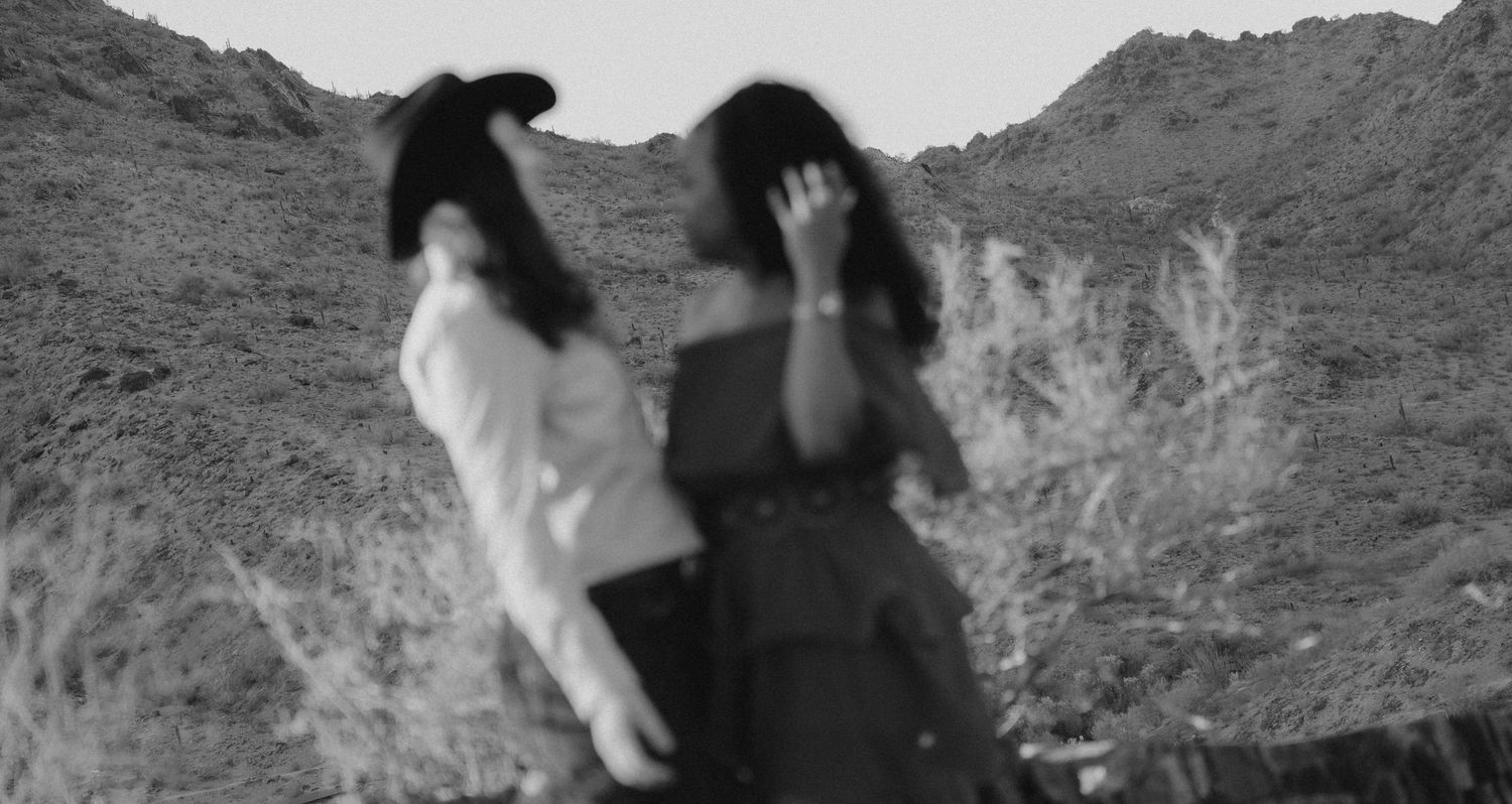 Artistic black and white photo of two figures with flowing hair against mountain landscape.