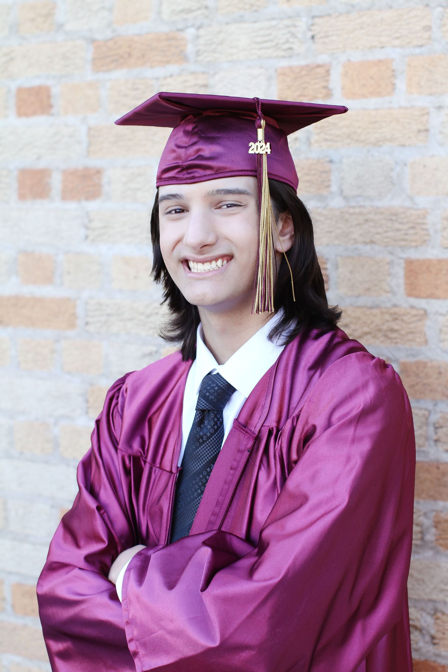 Graduate in maroon cap and gown smiling confidently against a brick wall.