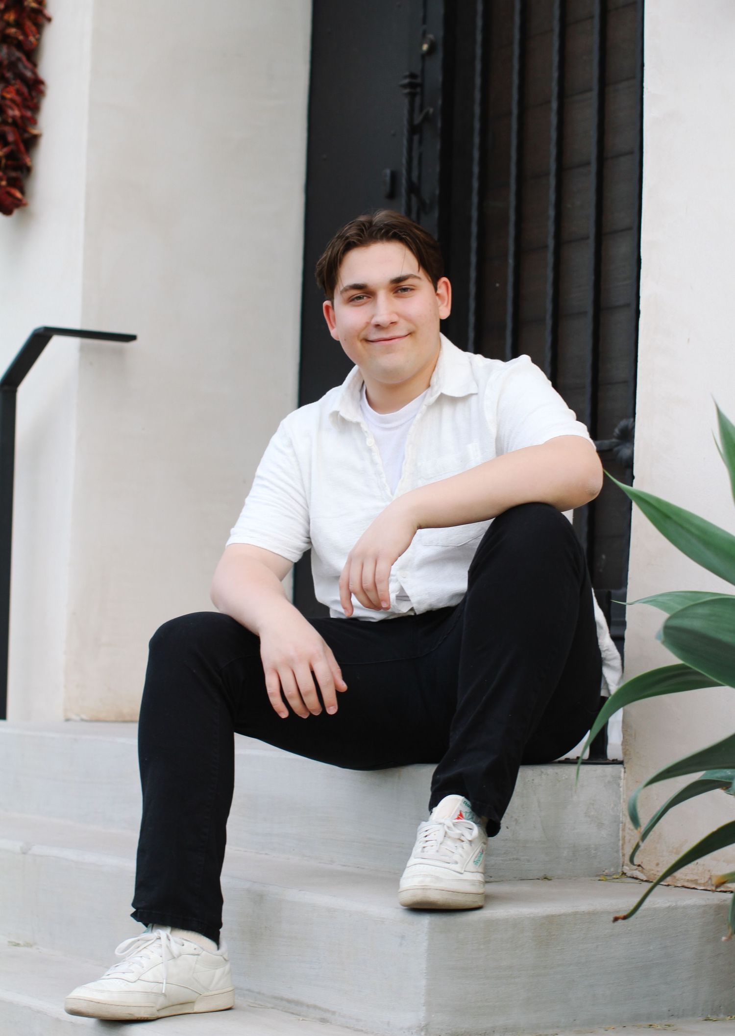 Casual portrait of person in white shirt sitting on concrete steps near plants.