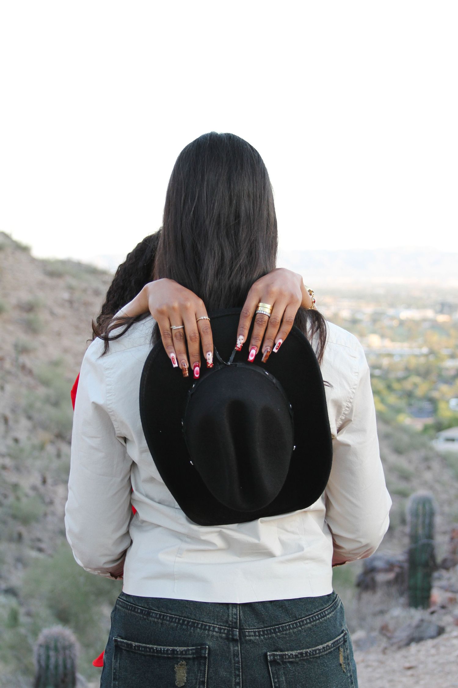 Person in white top holding black cowboy hat against desert backdrop.