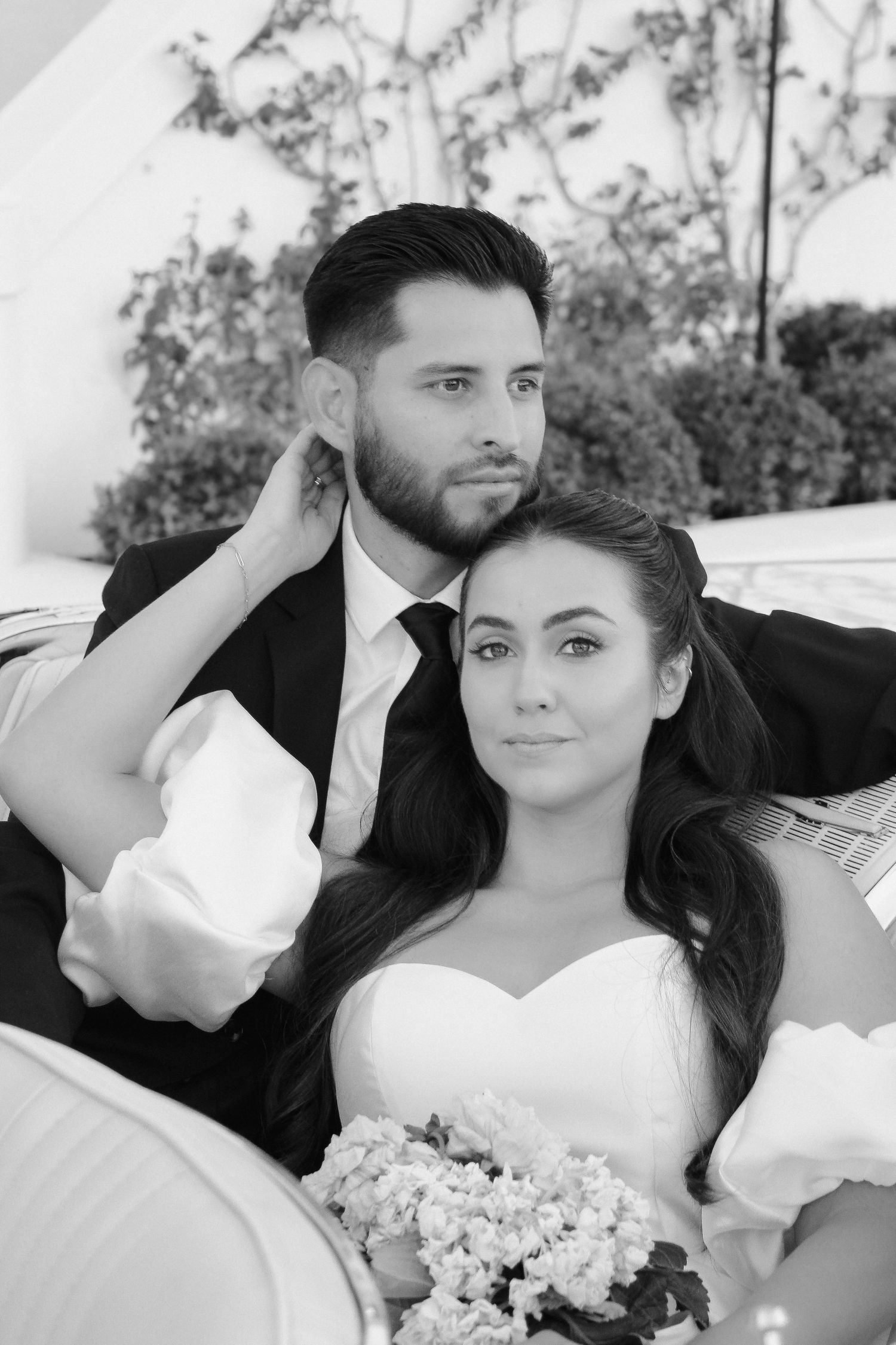 Black and white portrait of wedding couple in formal attire with bride holding floral bouquet.