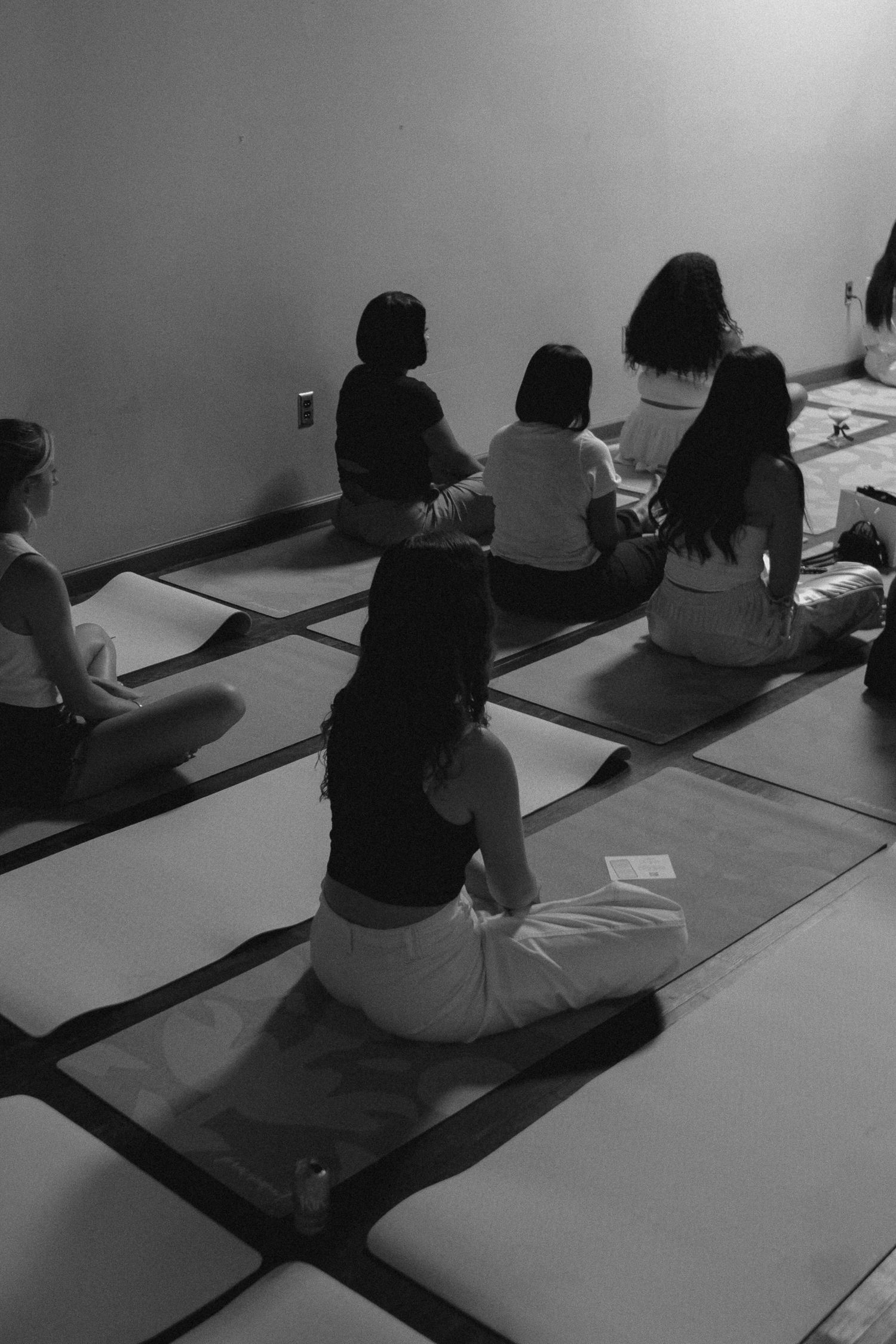Black and white photo of women sitting cross-legged on yoga mats in a meditation class studio.