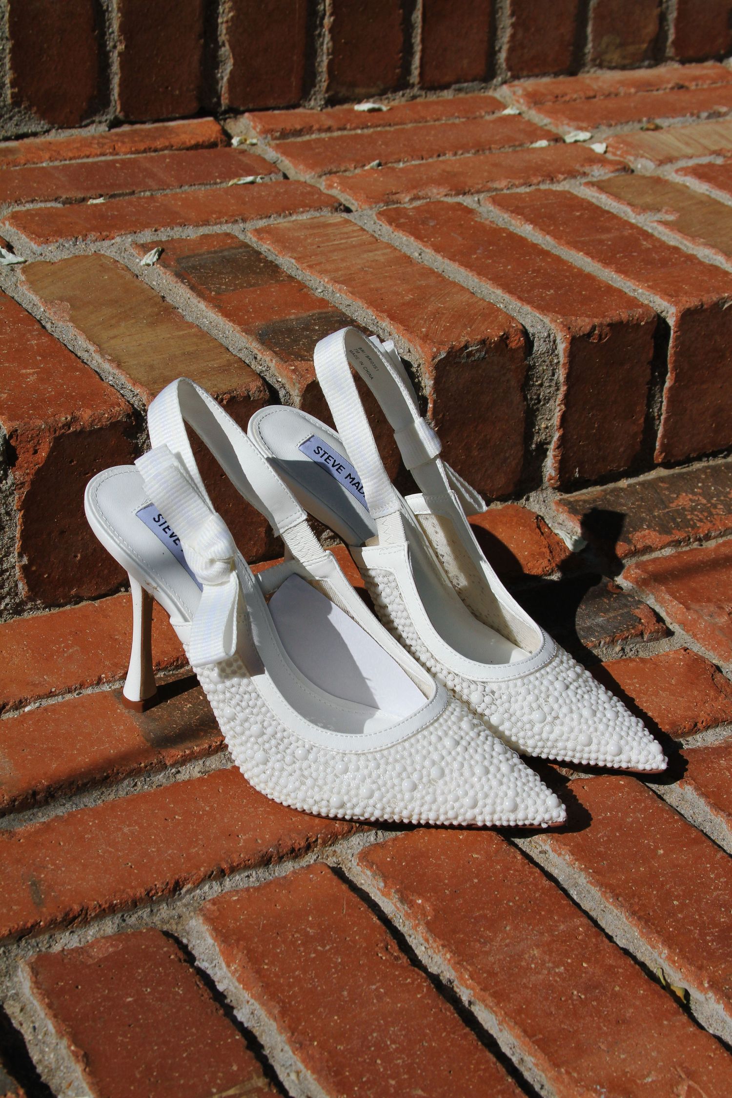 Elegant white beaded bridal heels with pointed toes arranged on red brick steps. Tyler Garlej Photography