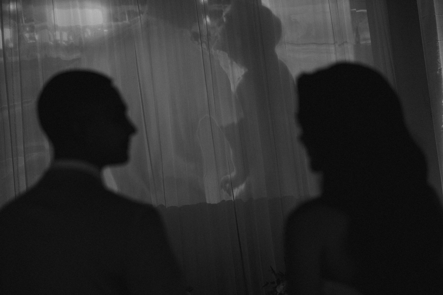 Tyler Garlej Photography - A series of silhouettes of people standing in front of a bright window with rain falling outside.