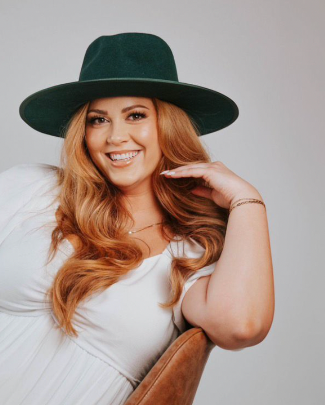Studio portrait featuring green wide-brim hat and casual styling against white background.