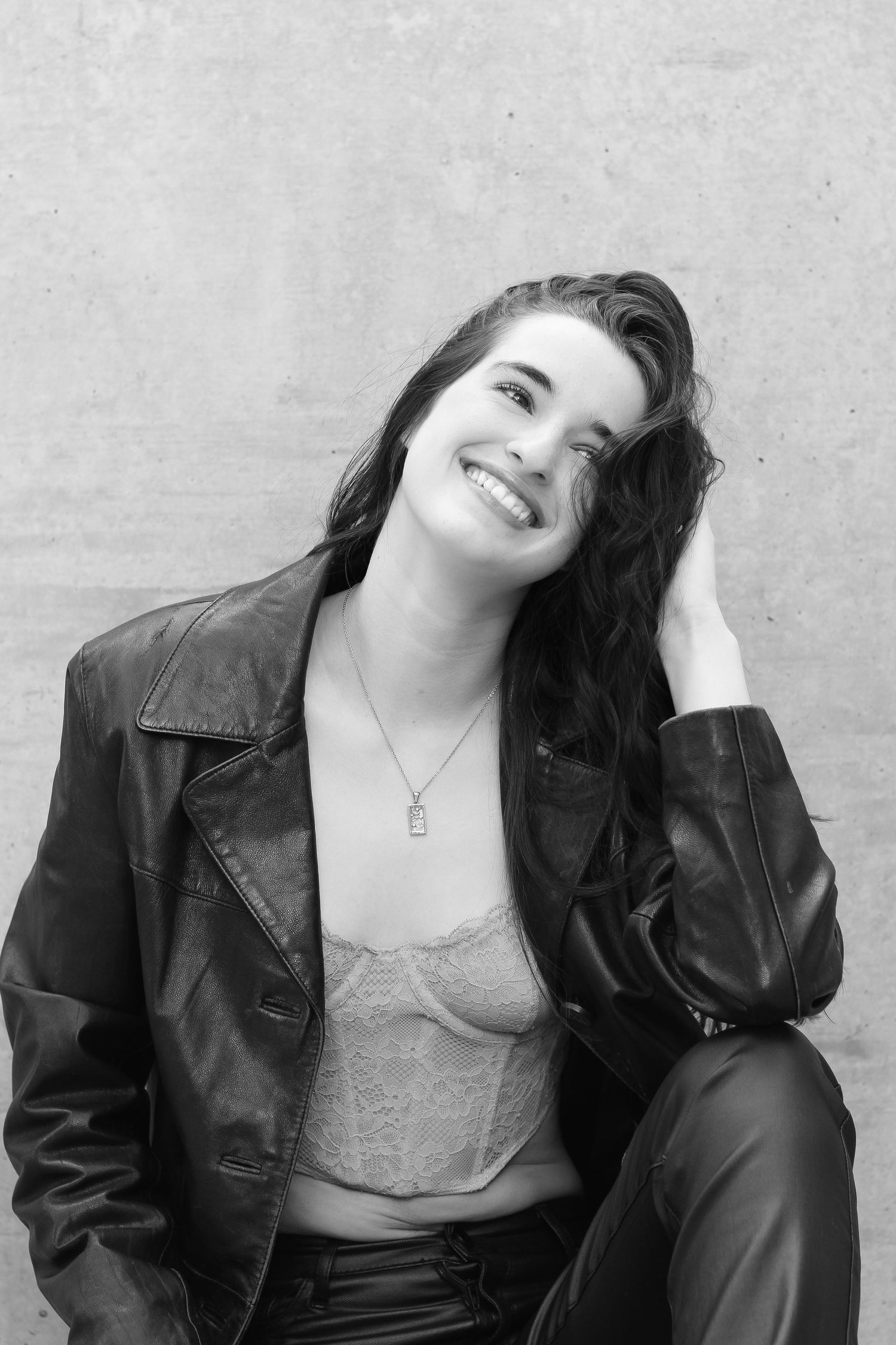 Black and white portrait of a model in leather jacket against concrete wall.