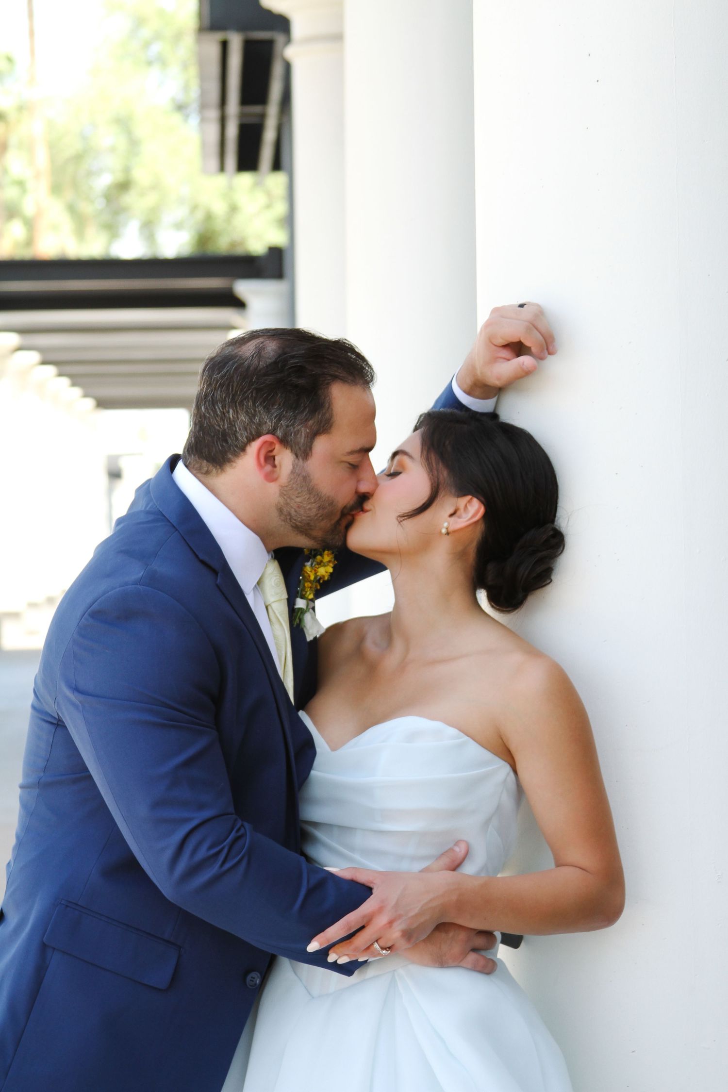 Intimate wedding kiss against a white pillar in classic bride and groom attire.