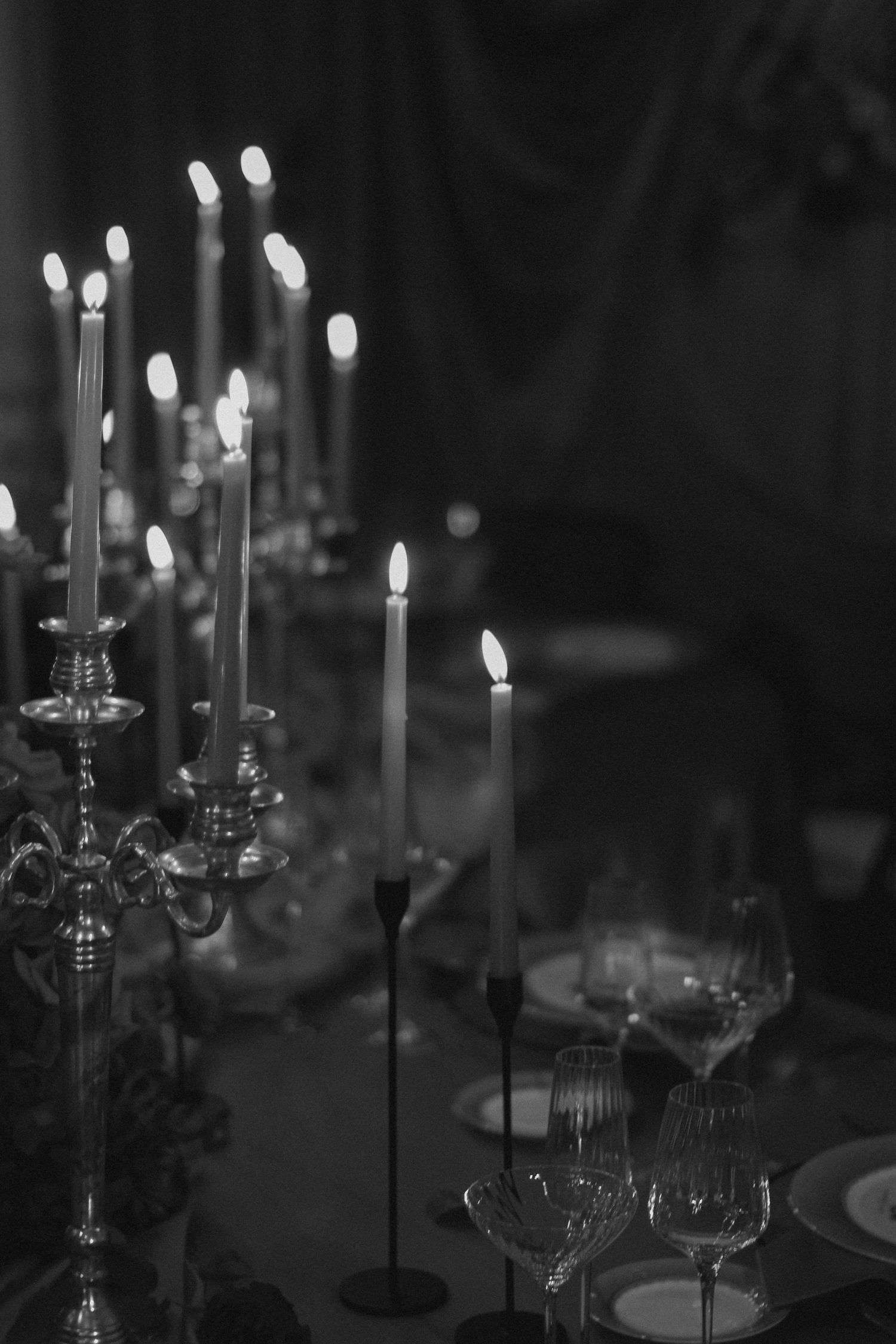 Elegant table setting with lit candelabras and crystal glasses in moody black and white.
