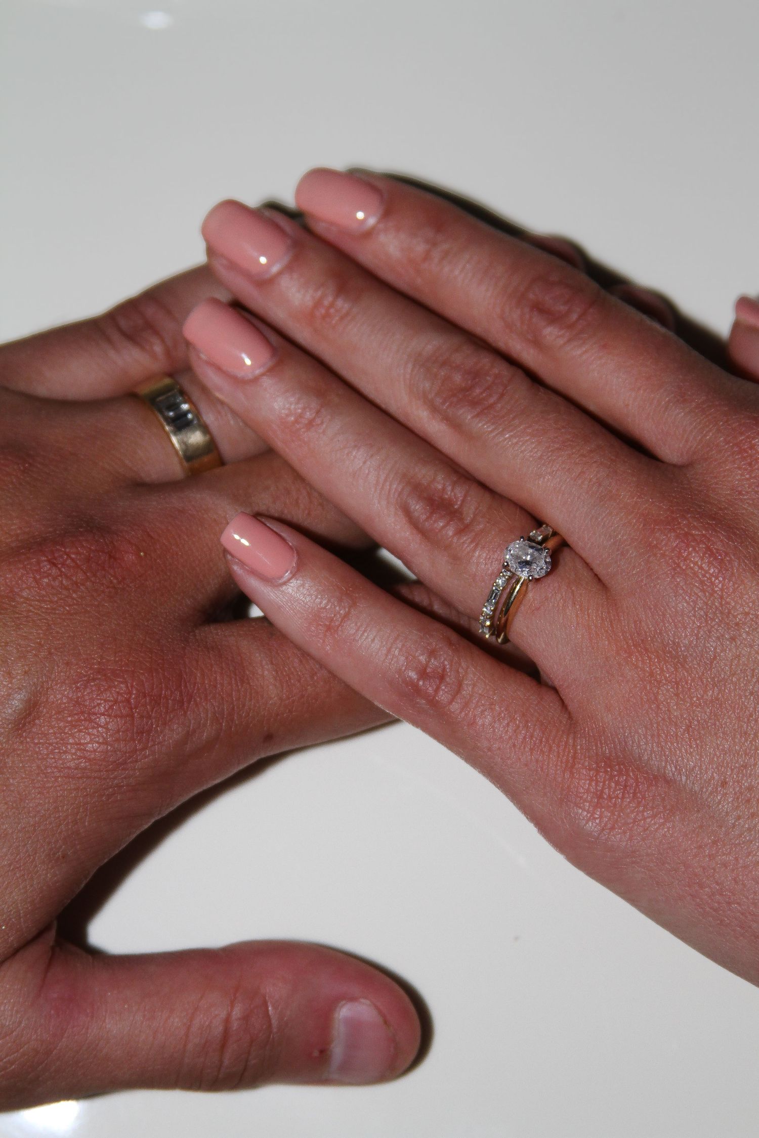 Close up of hands displaying wedding rings against light background.