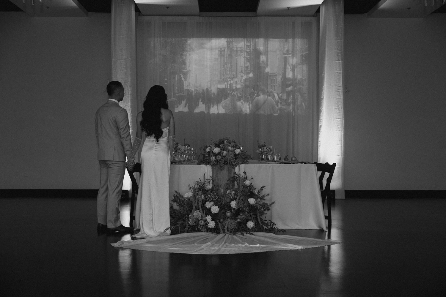 Black and white photo of bride and groom standing before floral altar display at wedding ceremony.