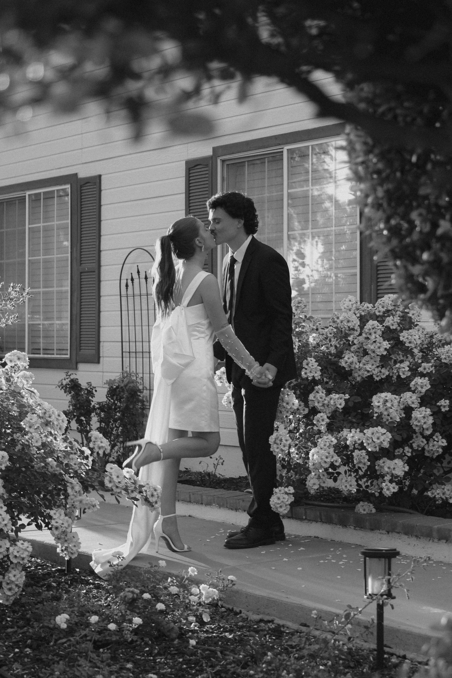Romantic black and white silhouettes share an intimate moment among blooming hydrangea bushes outside a white house.