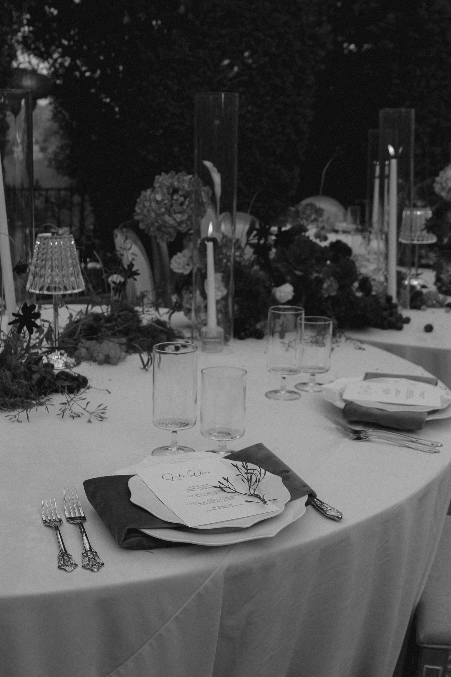 Black and white photo of an elegant wedding table setting with candles, floral arrangements, and place cards.