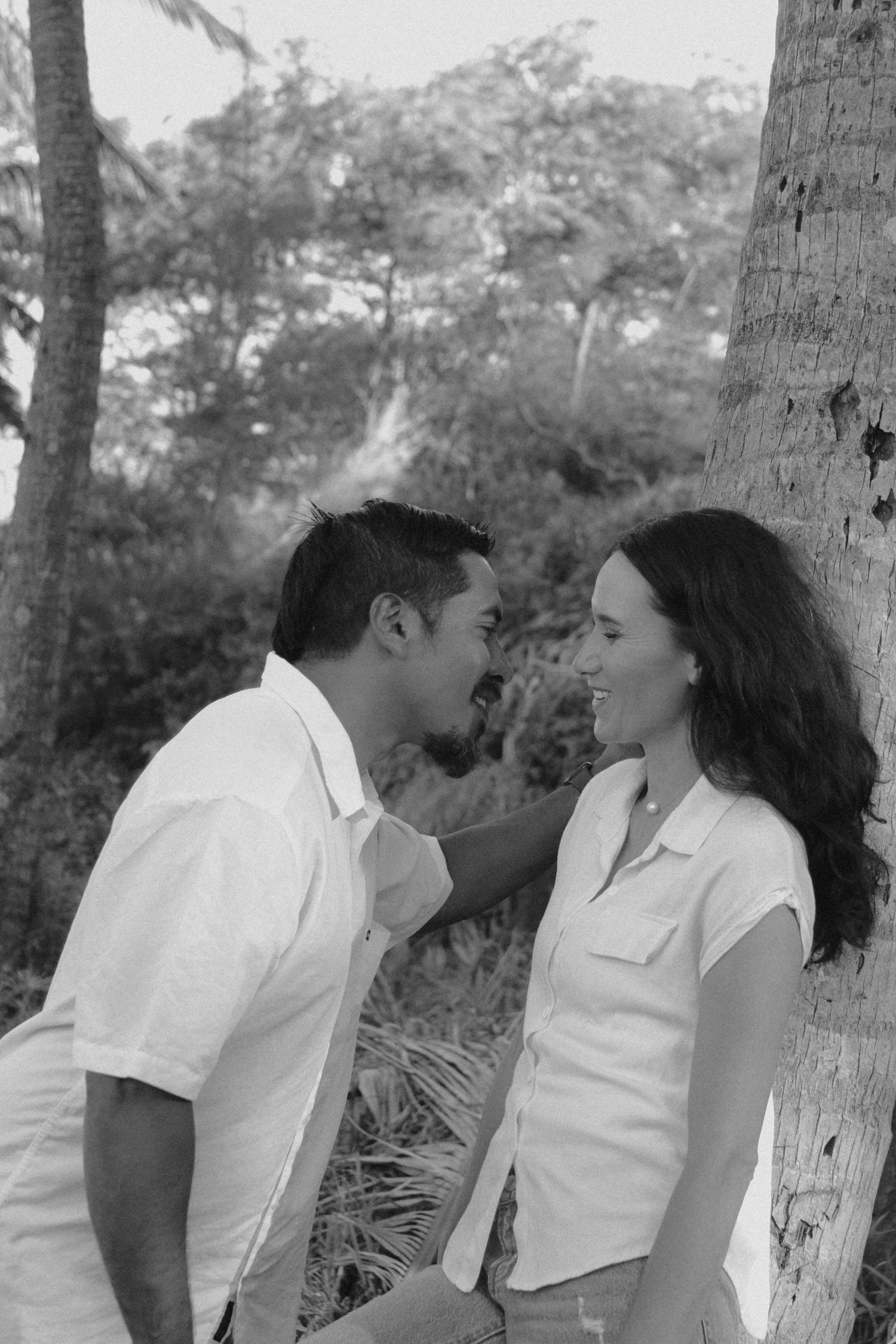 Black and white sequence of a romantic couple in white shirts sharing a kiss against a tree trunk in a natural setting.
