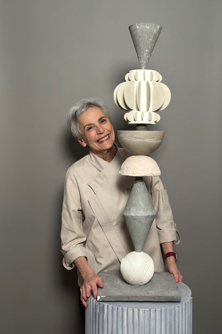 Artist poses playfully with handcrafted ceramic vessels and sculptures in a minimalist studio setting.