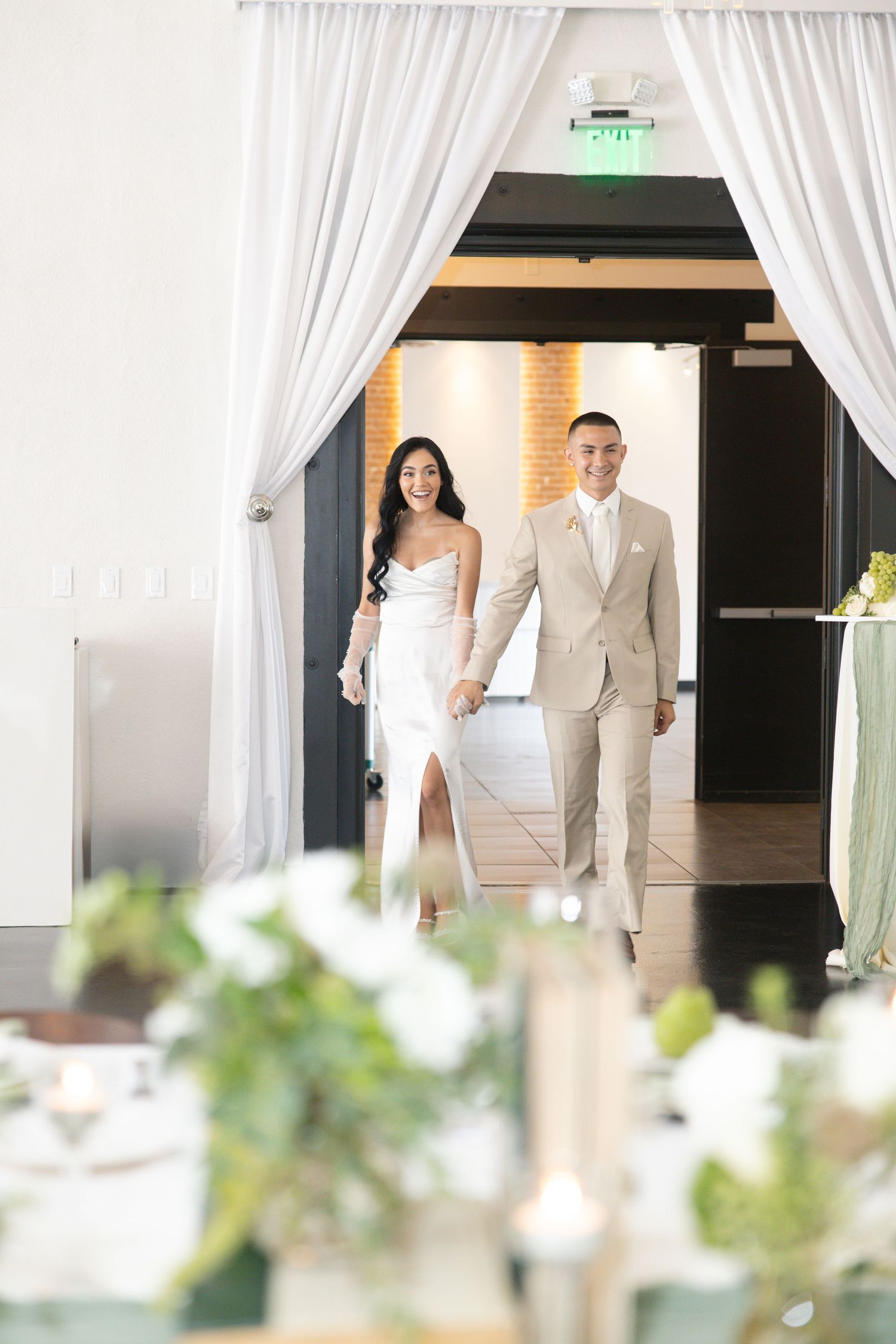 Bride and groom entering wedding reception hand in hand through draped white curtain doorway.