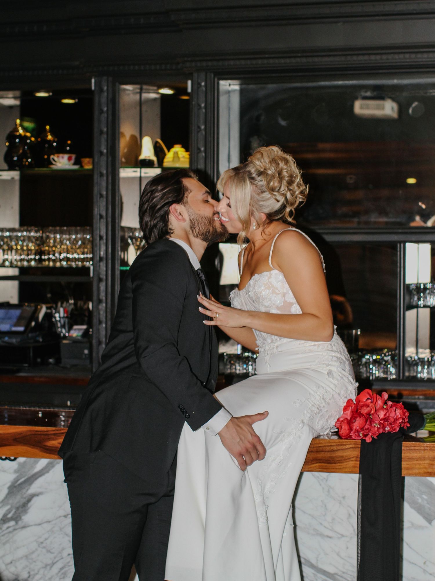 A couple shares a romantic moment near a marble bar counter during their wedding celebration.