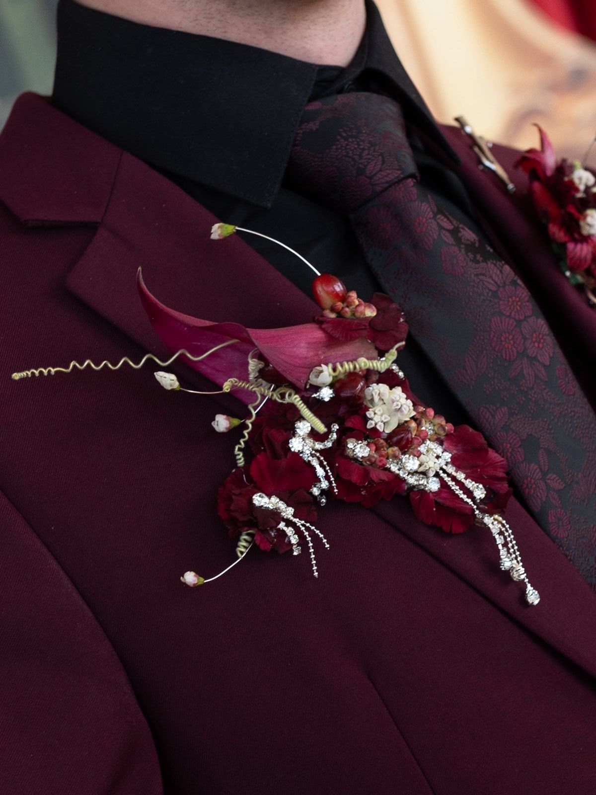 Close-up of a burgundy suit lapel adorned with an elegant dark red floral boutonniere with pearl accents.