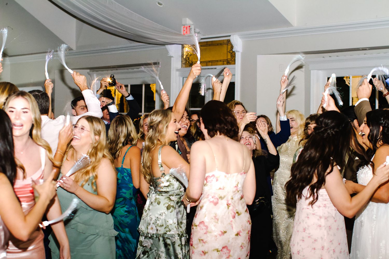A group of people dancing and celebrating at a wedding reception with their hands raised in the air.