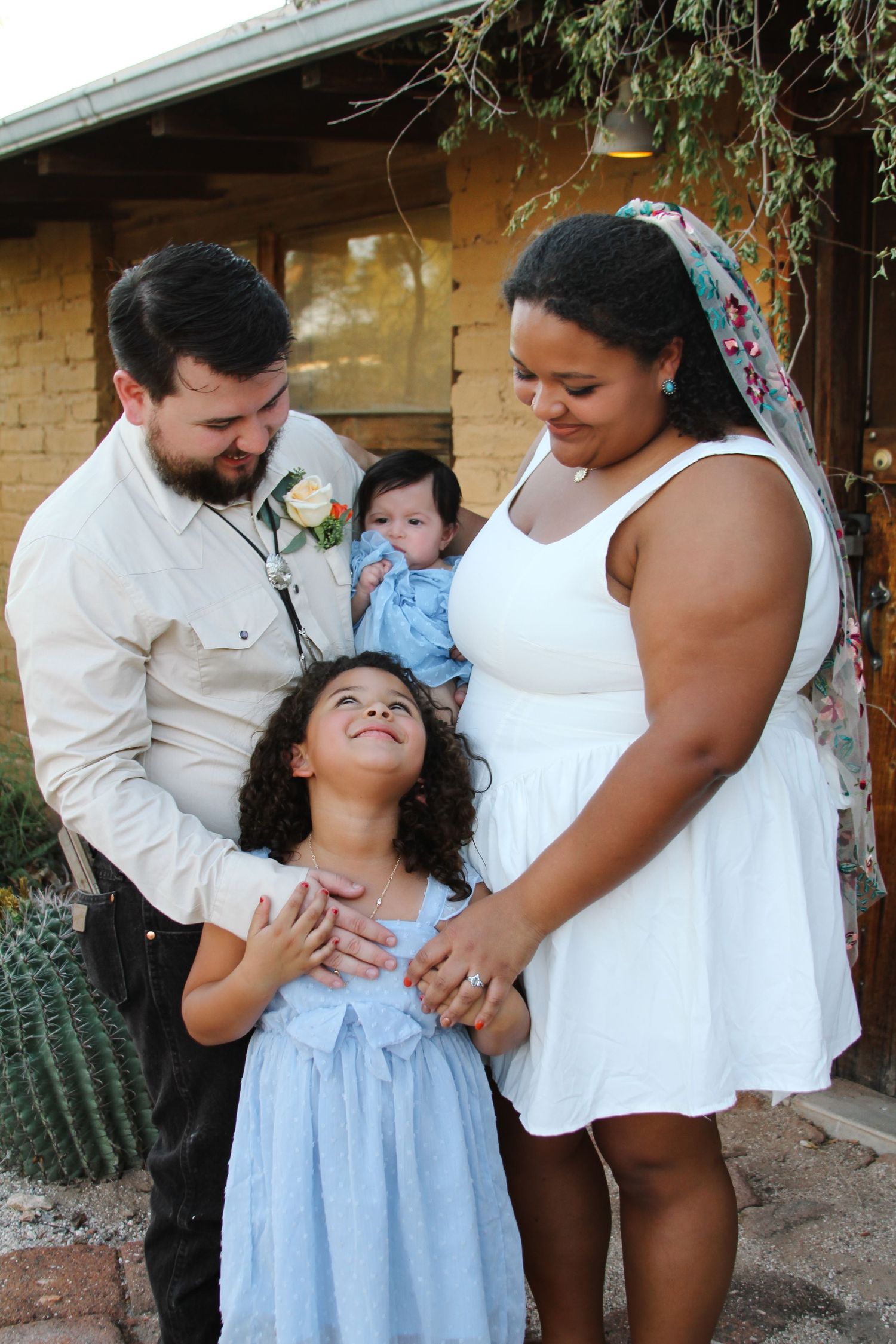 Family shares joyful moment together in desert garden setting with adobe walls.