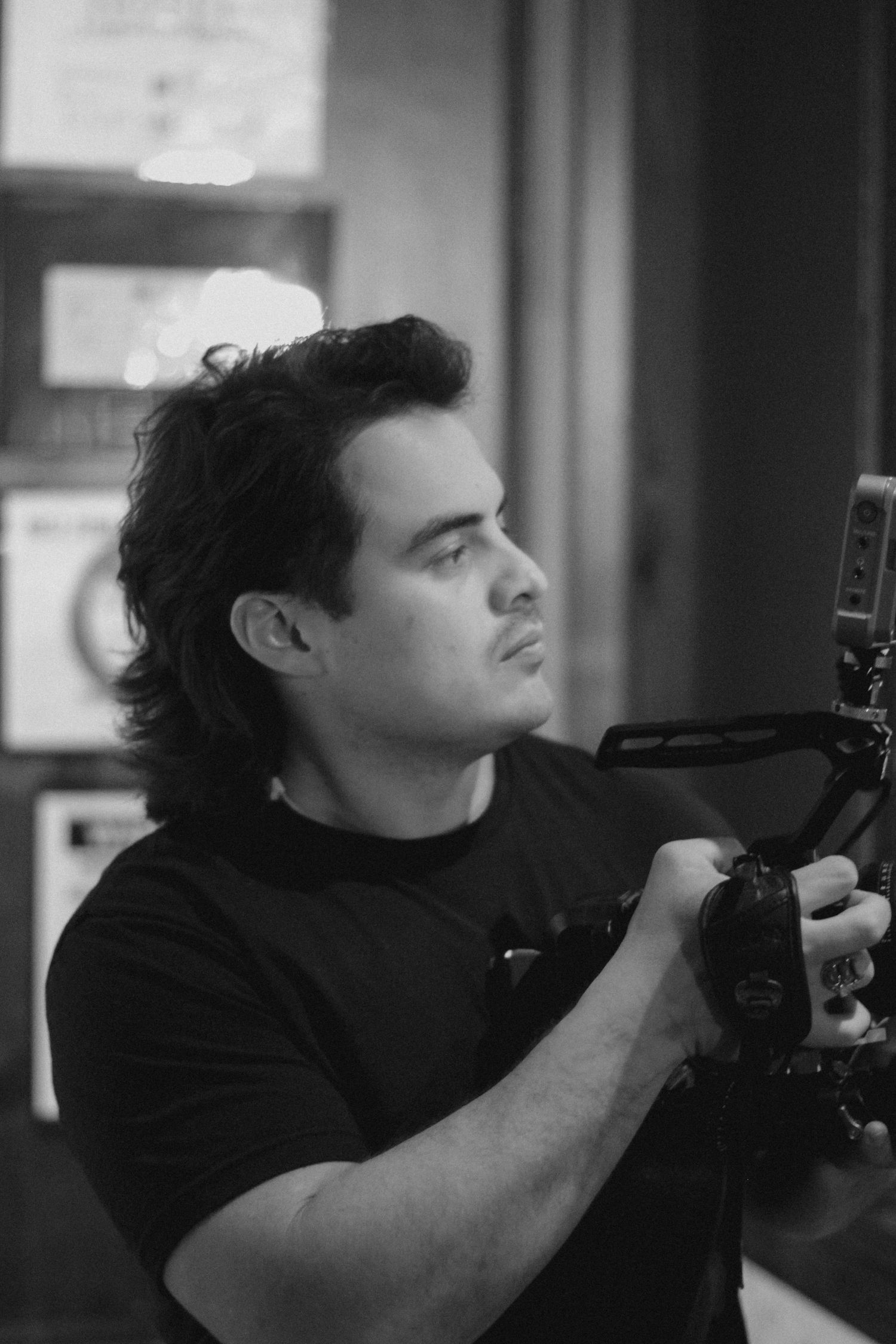Black and white photo of a young man holding a professional camera, captured in a cinematic side profile shot.
