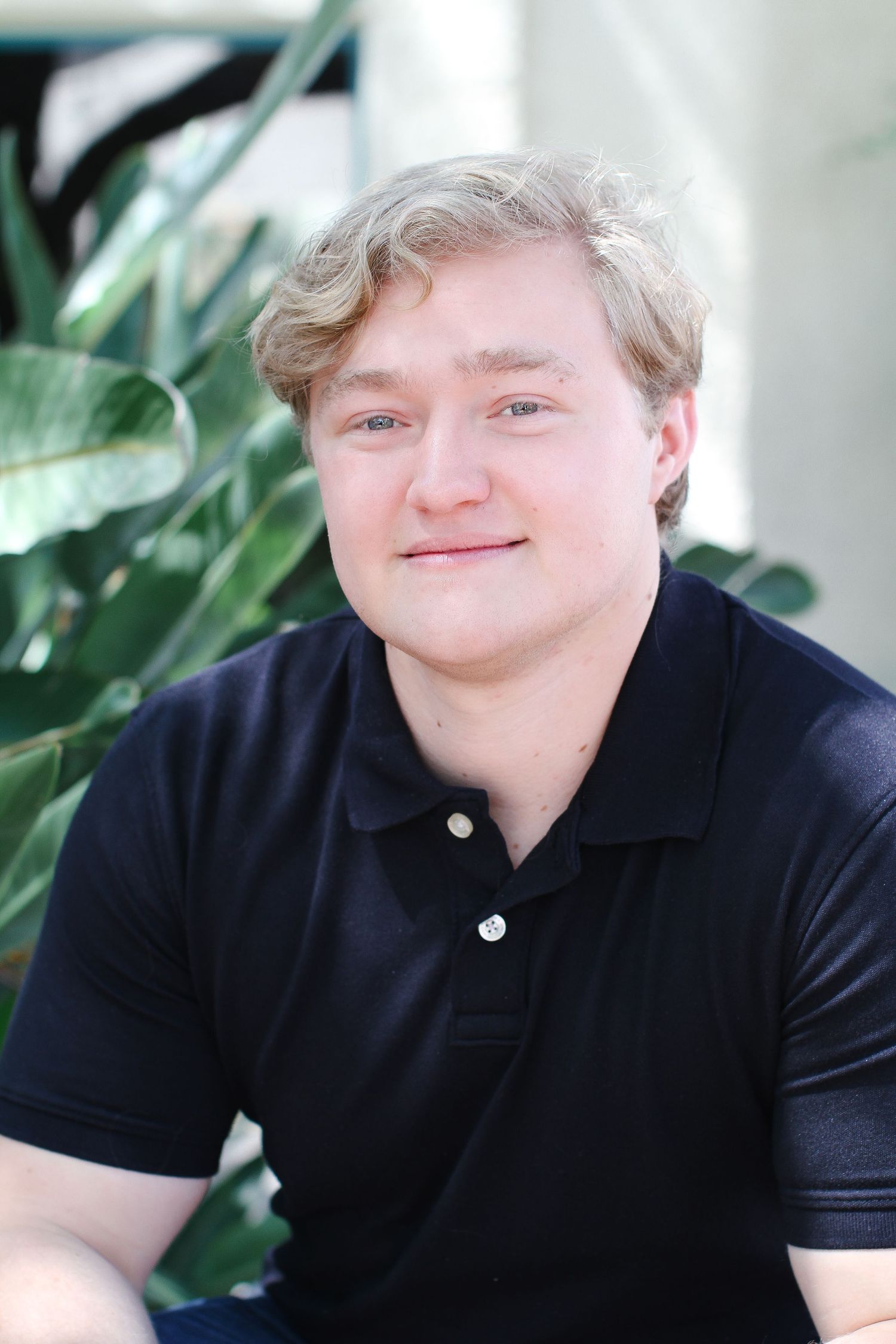 Portrait of a person in a navy polo shirt sitting by tropical plants.
