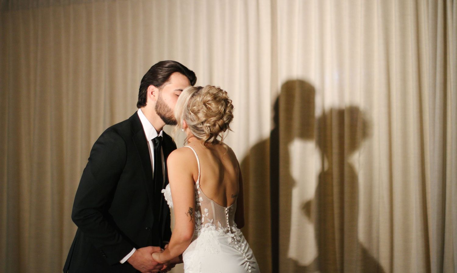 Tyler Garlej Photography - A romantic wedding couple shares intimate kisses in front of an elegant beige curtain backdrop.