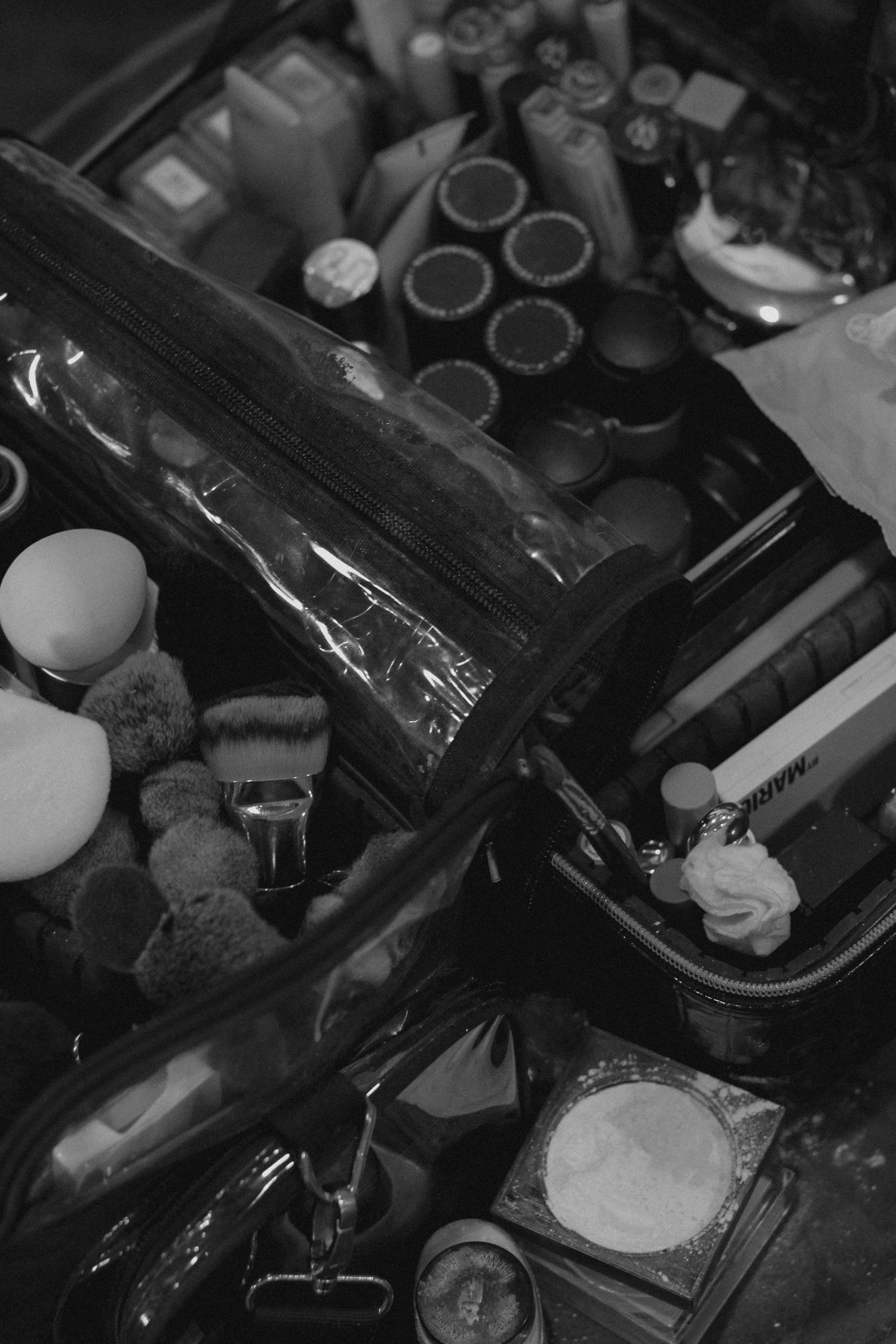 Black and white close-up of makeup products and cosmetics organized in a drawer or container.