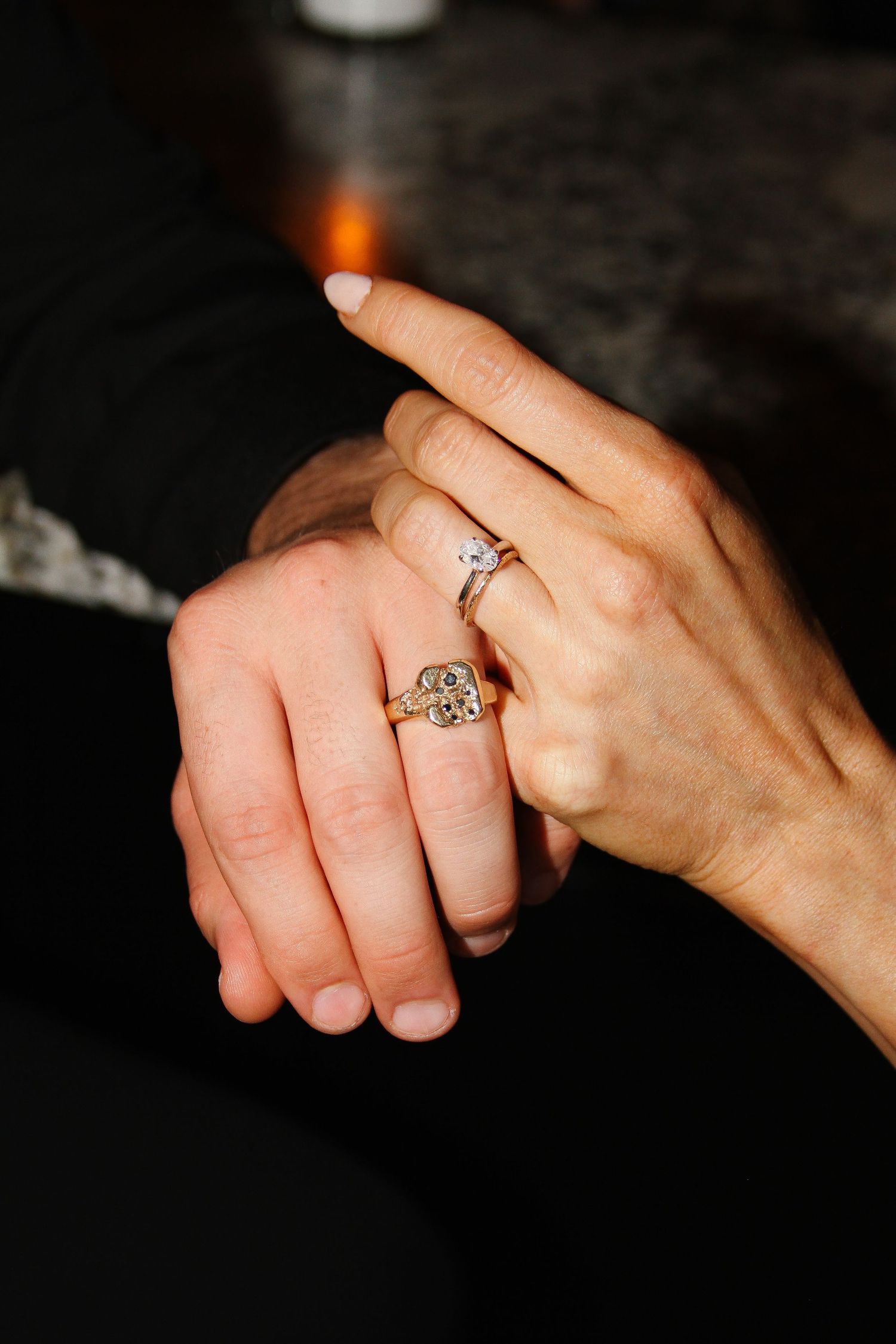 Close-up of hands showing engagement and wedding rings in romantic lighting.