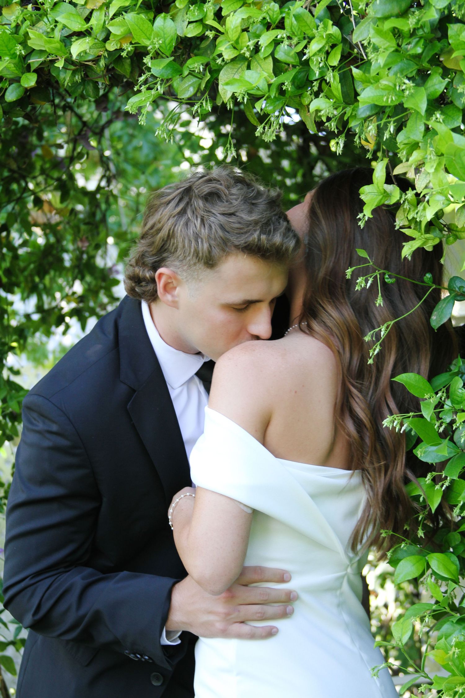 An intimate moment between newlyweds embracing beneath green foliage.