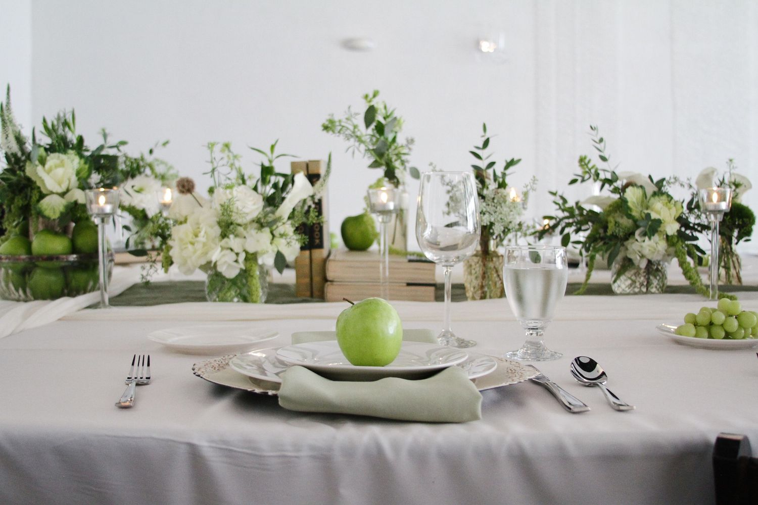 Elegant wedding table setting with green apple centerpiece, white floral arrangements, and gray linen tablecloth.