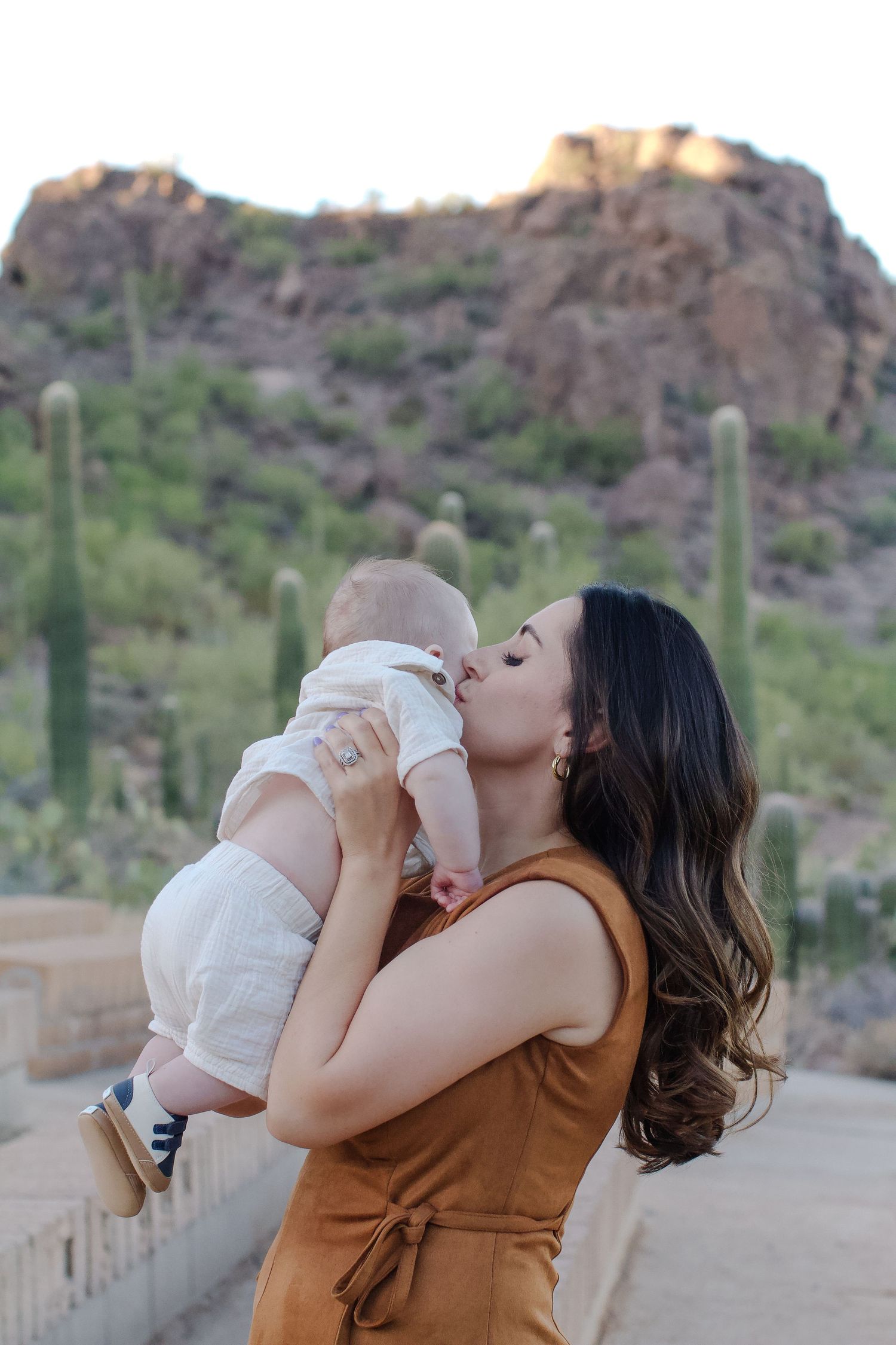 A series of photos showing a person in a brown vest kissing a baby against a desert mountain backdrop.