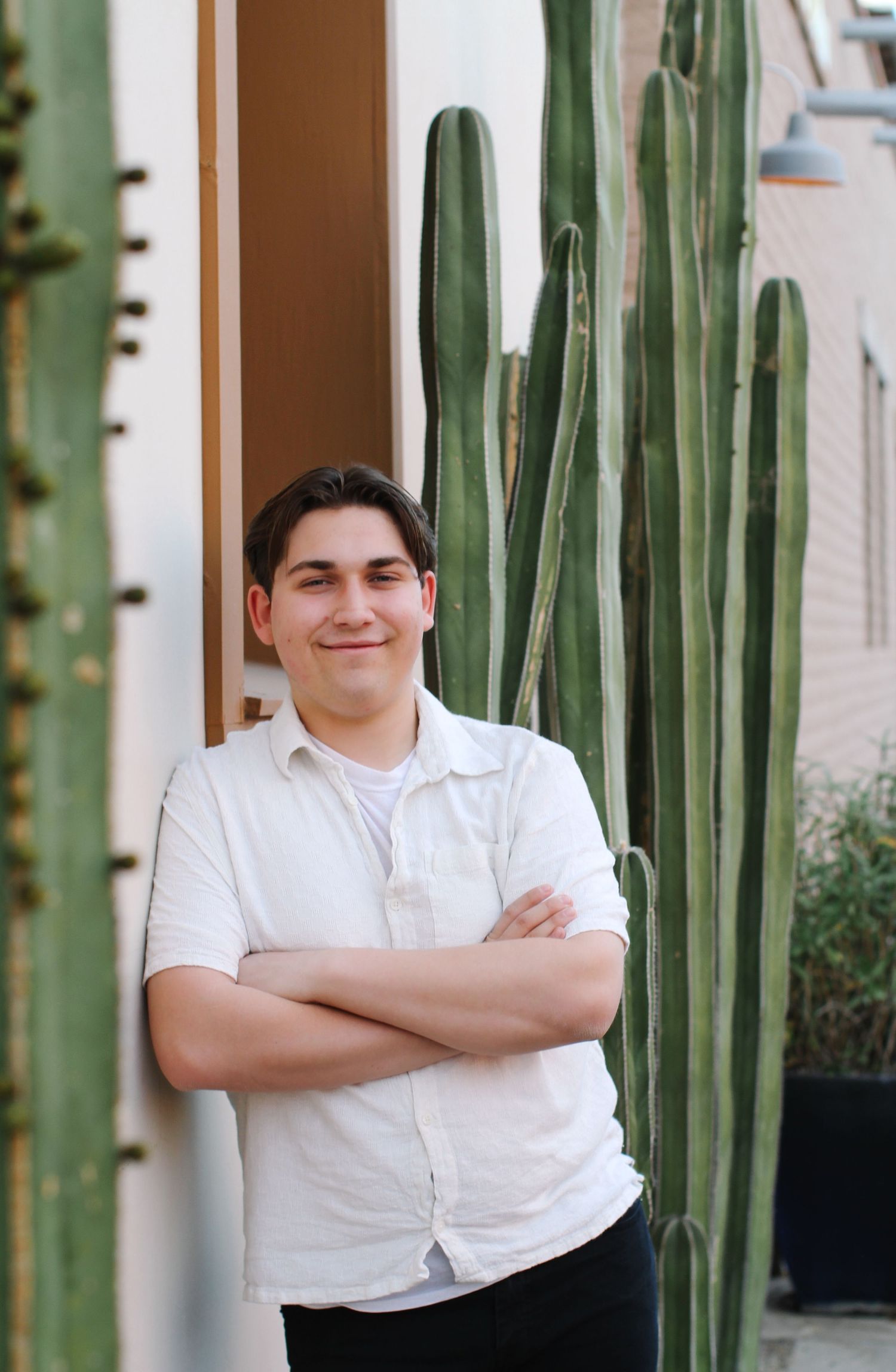 Portrait of person in white shirt standing next to tall cactus plants.