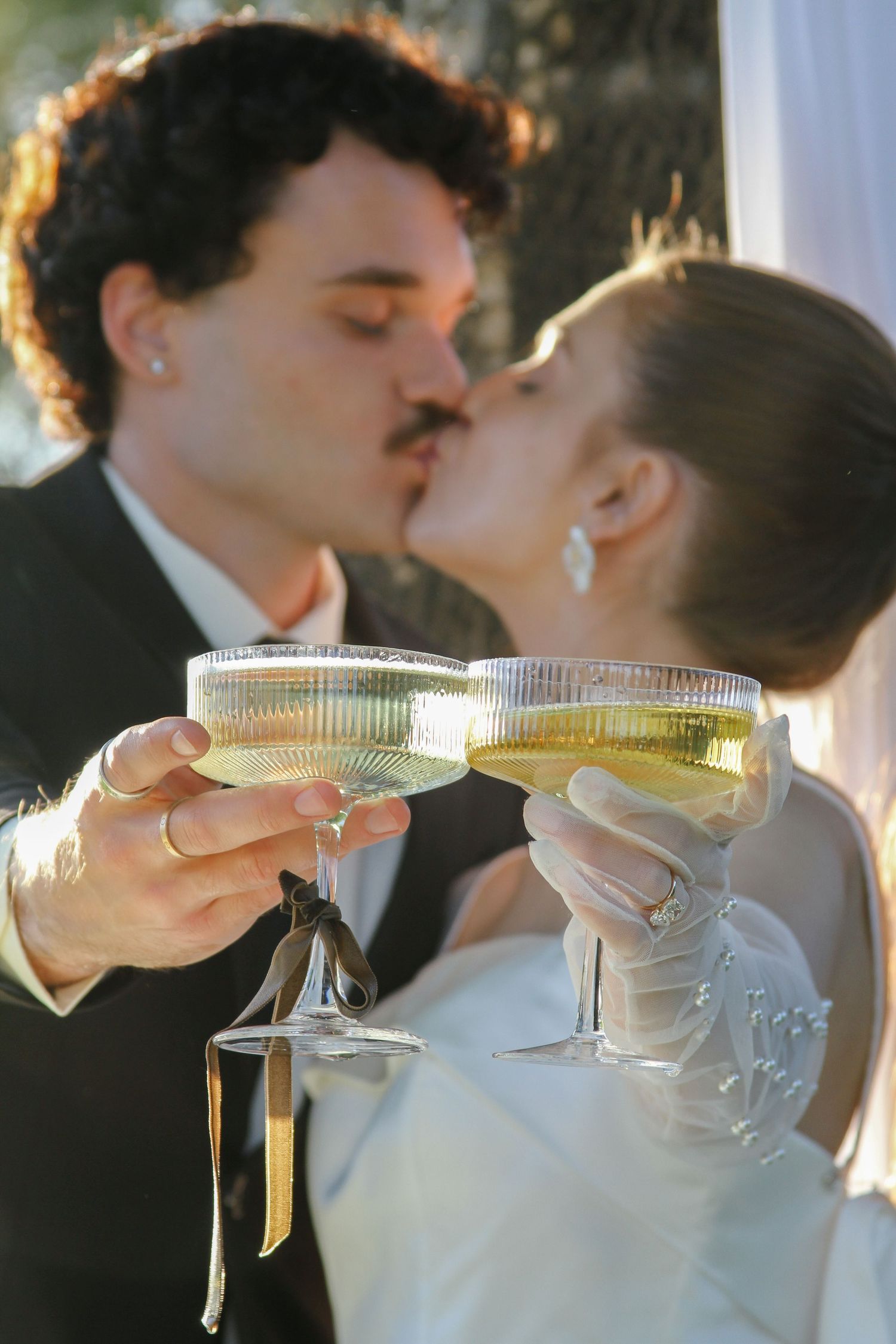 Bride and groom kissing while holding champagne glasses at their wedding celebration.