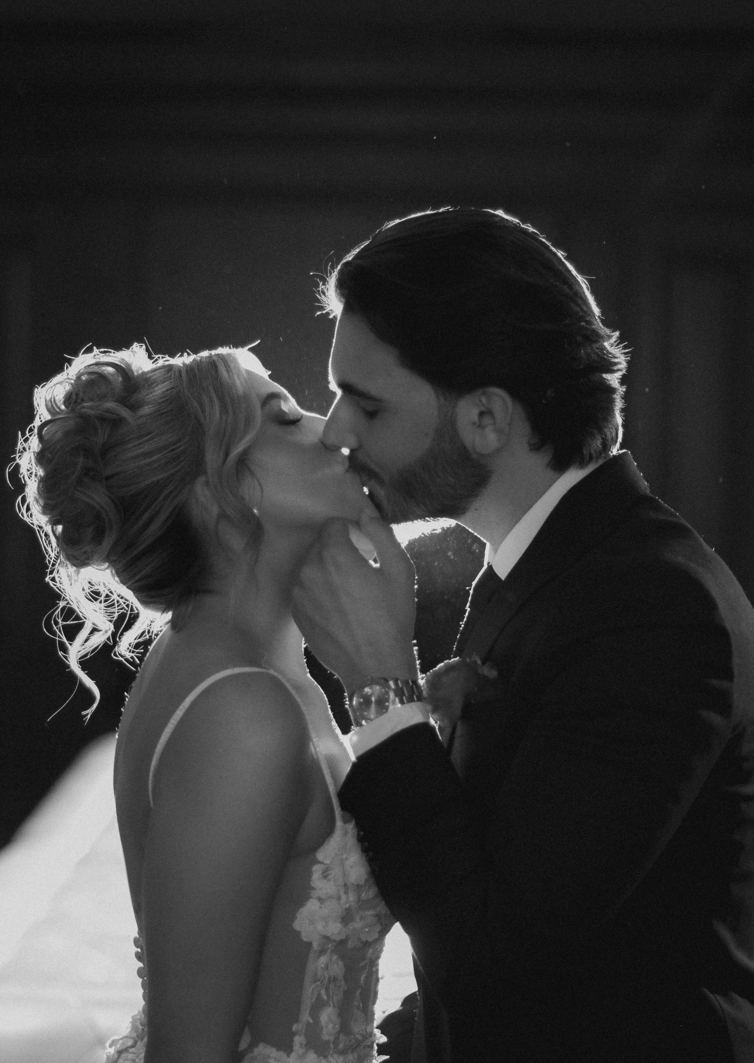 Tyler Garlej Photography - A romantic silhouette of a couple sharing a kiss during their wedding ceremony, backlit with dramatic lighting.